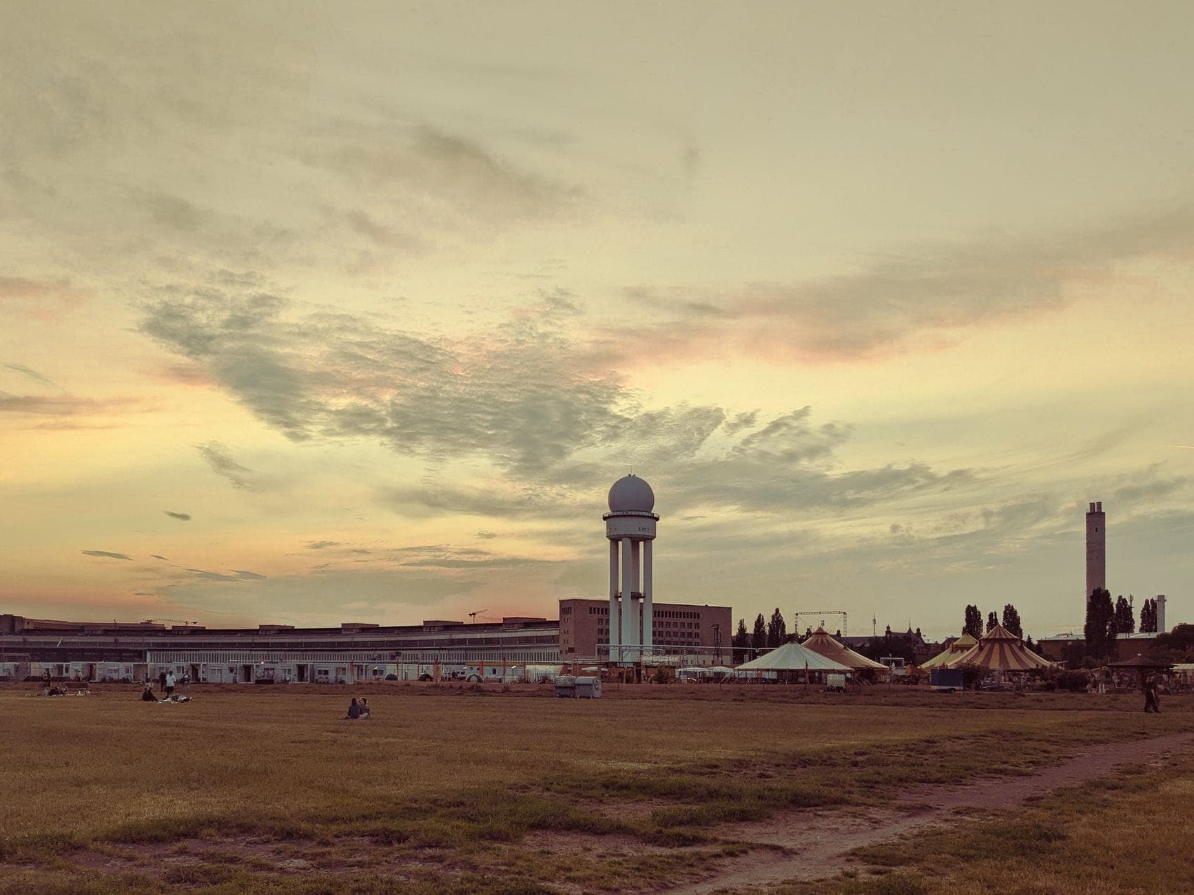 Tempelhofer Feld al atardecer, con personas descansando en el césped y la histórica terminal al fondo bajo un cielo dramático.