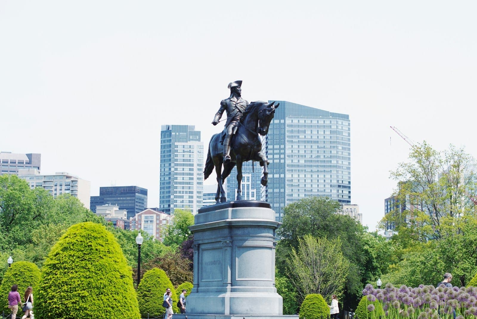 La statue de George Washington dans le Boston Public Garden entourée d'arbustes taillés et de bâtiments modernes de la ville par une journée lumineuse.
