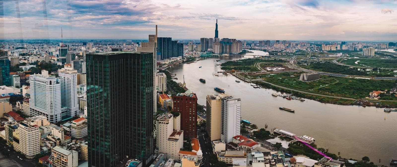 Pemandangan udara panoramik cakrawala Ho Chi Minh City di sepanjang Sungai Saigon dengan gedung pencakar langit, padatnya kawasan perkotaan, dan langit senja yang dramatis.