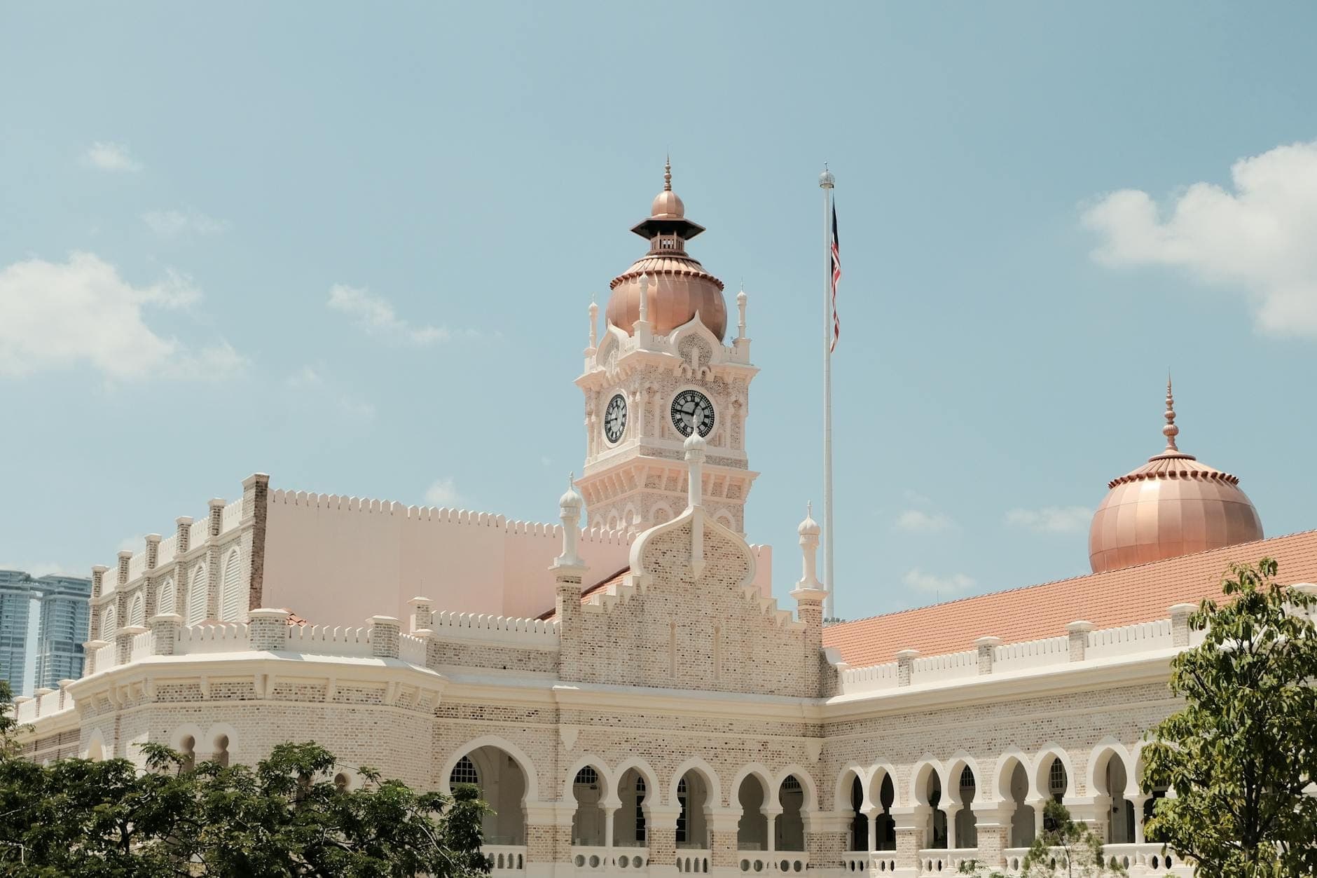 Здание Sultan Abdul Samad в Куала-Лумпур с медным куполом и часовой башней на фоне ясного голубого неба в мягком солнечном свете.