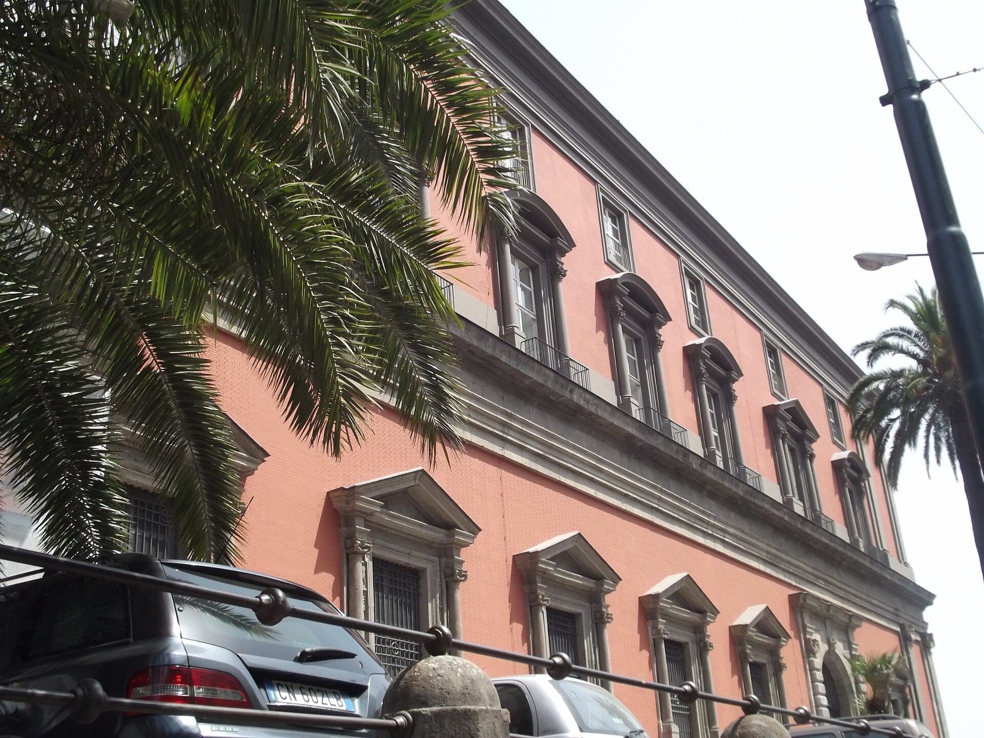 Fachada de um grande e elegante edifício rosa com janelas amplas e palmeiras na frente, em Nápoles, Itália
