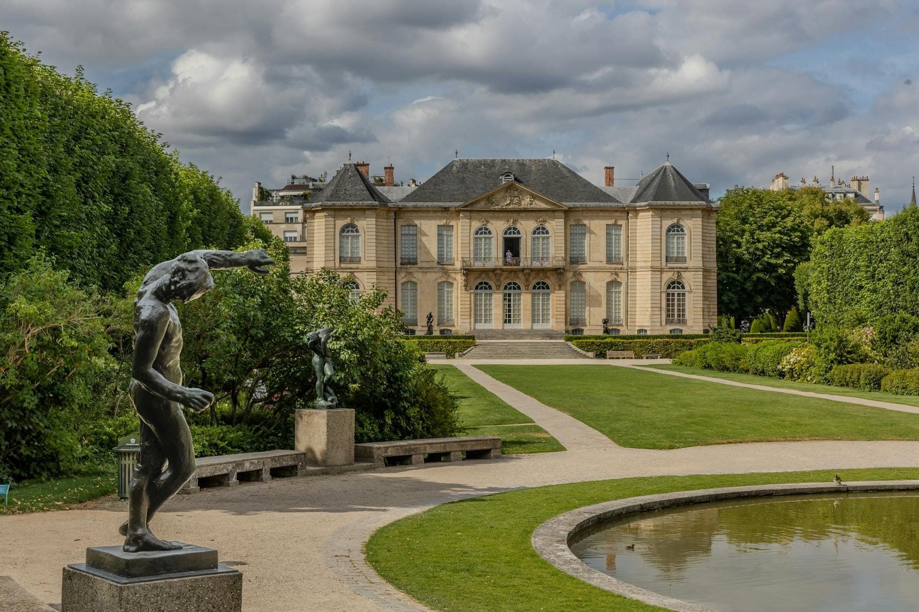 Eleganter Blick auf das Musée Rodin in Paris, mit Skulpturengärten, Gehwegen, Statuen und dem Museumsgebäude unter einem dramatischen Himmel.