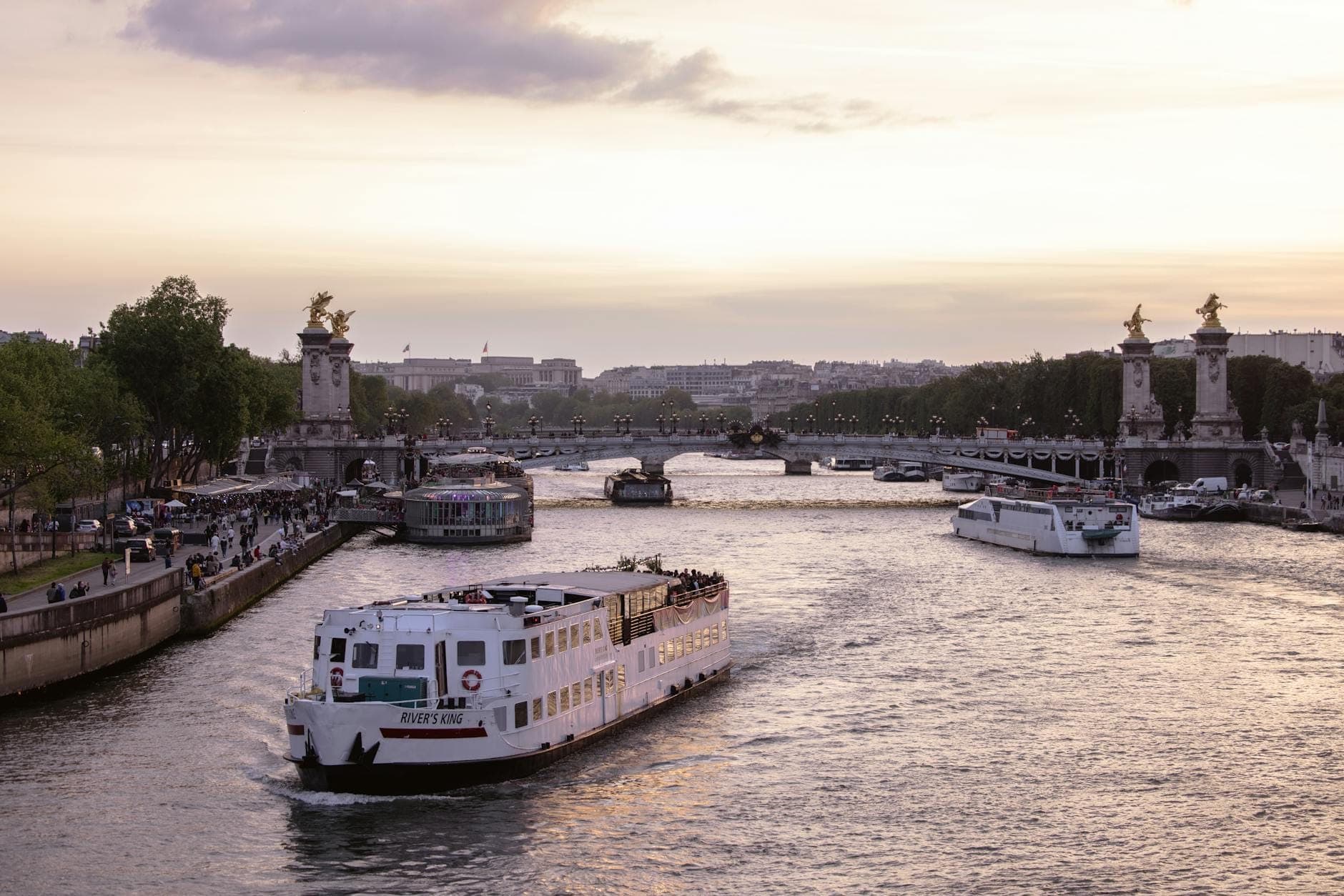 Ein Ausflugsboot fährt bei Sonnenuntergang auf der Seine entlang, während Pariser Brücken und Stadtsehenswürdigkeiten im Hintergrund sichtbar sind.