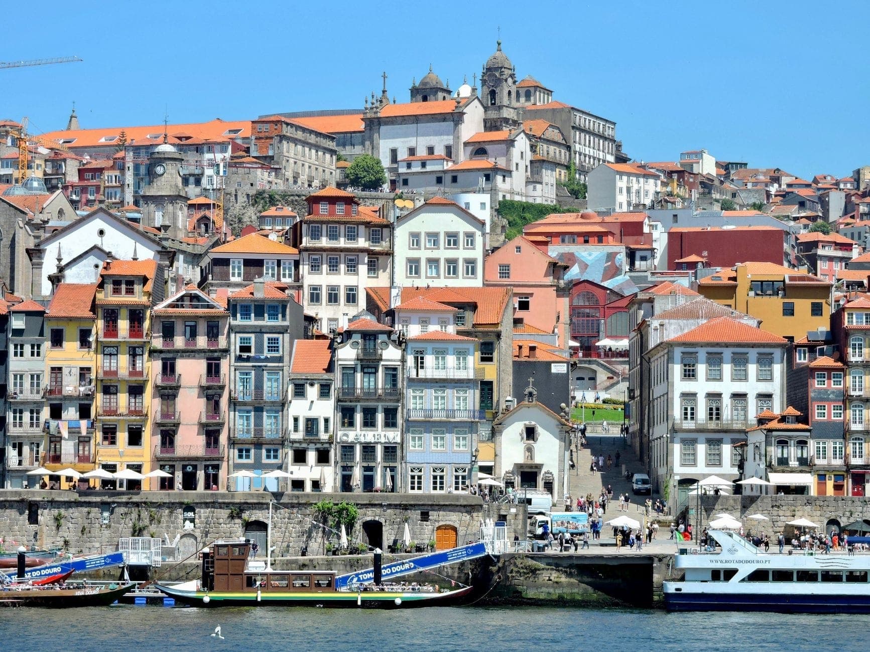 Kolorowe zabytkowe budynki wzdłuż rzeki Douro w wpisanej na listę UNESCO starówce Porto z łodziami i górującą katedrą.