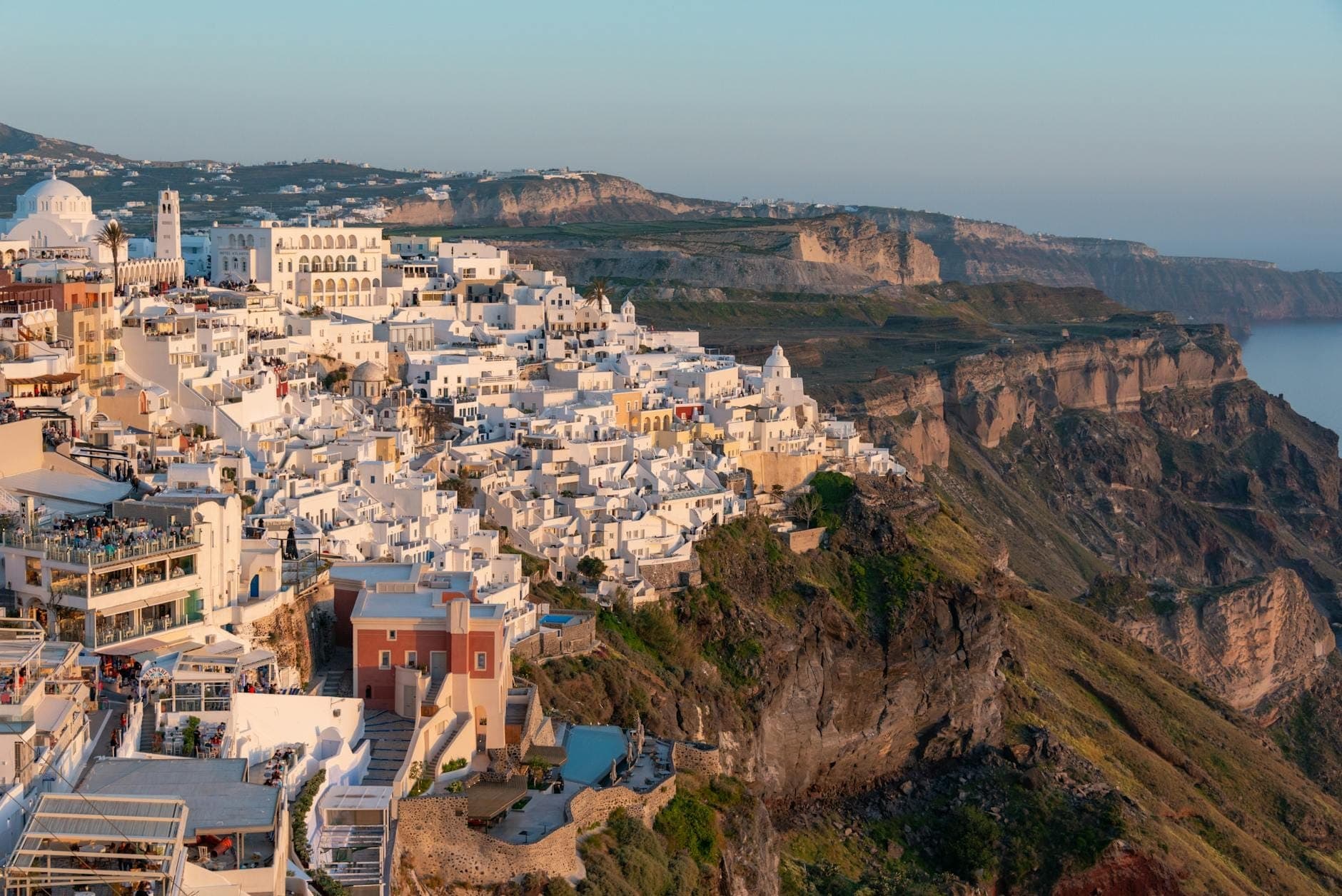 Vista ampia degli edifici bianchi sulle scogliere di Santorini che si affacciano sulla spettacolare caldera, con il mare e le ripide scogliere visibili.