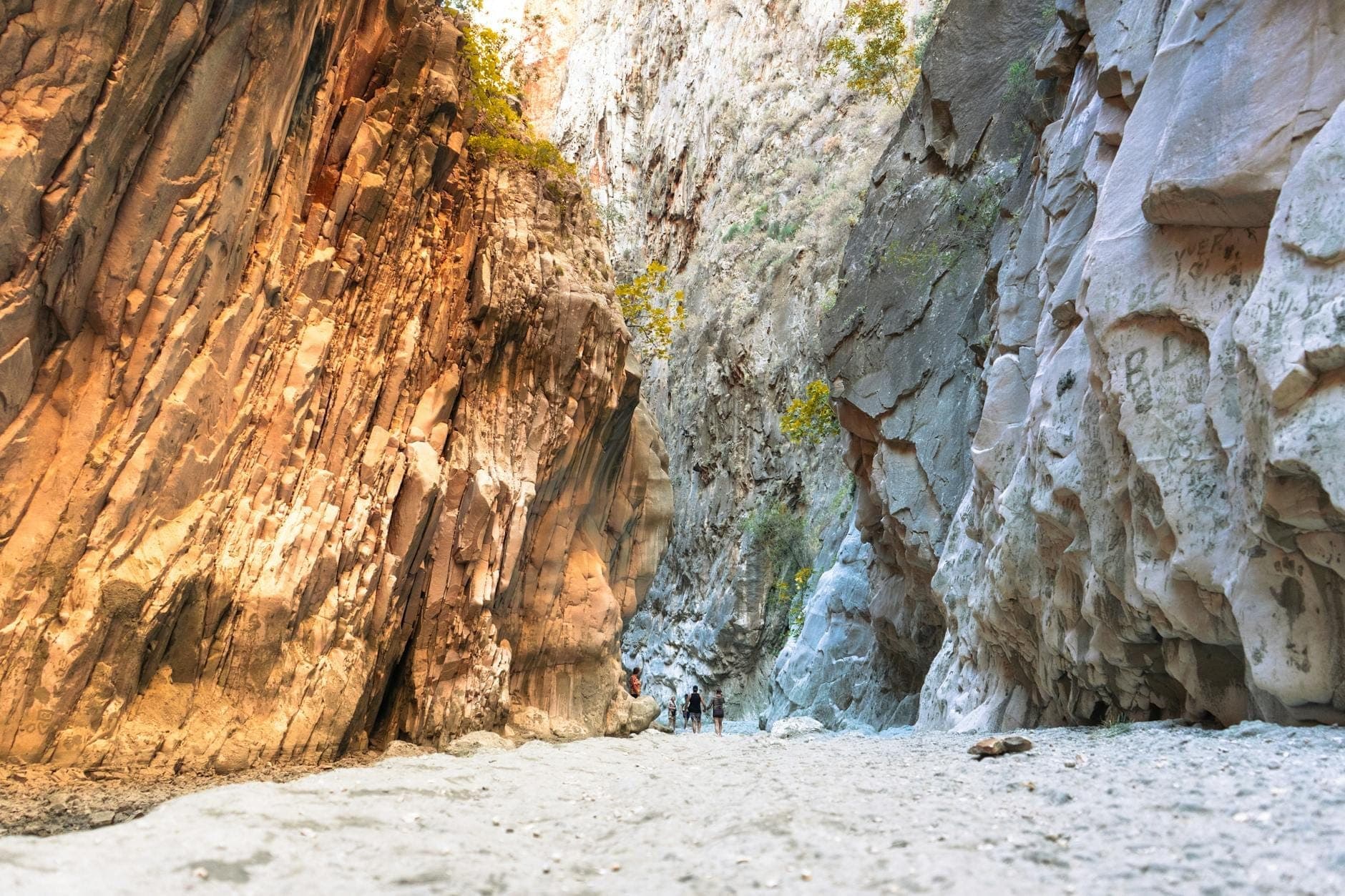 Vista de un dramático cañón rocoso con suelo arenoso y excursionistas caminando, que sugiere aventura al aire libre en el agreste paisaje de Sardinia.