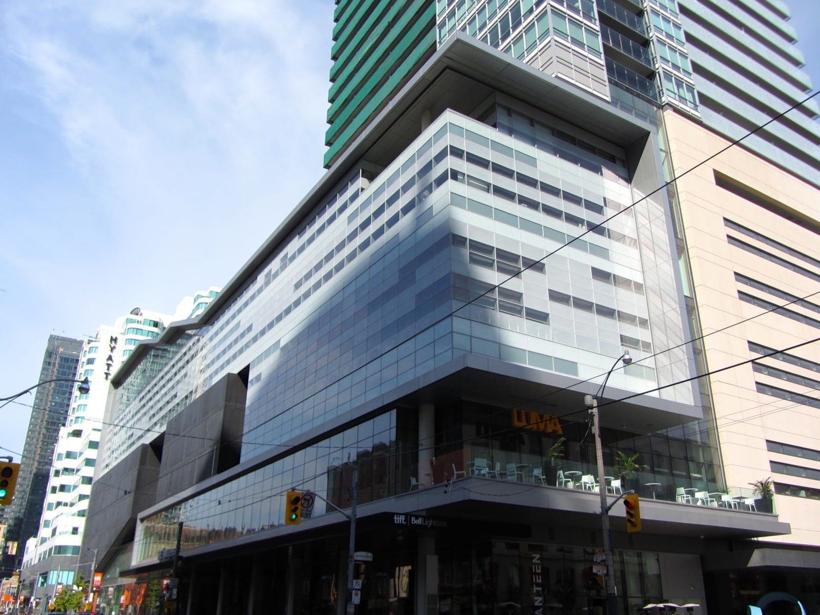 Vista esterna del TIFF Lightbox a Toronto, con architettura moderna in vetro e fili del tram sotto un cielo azzurro brillante.
