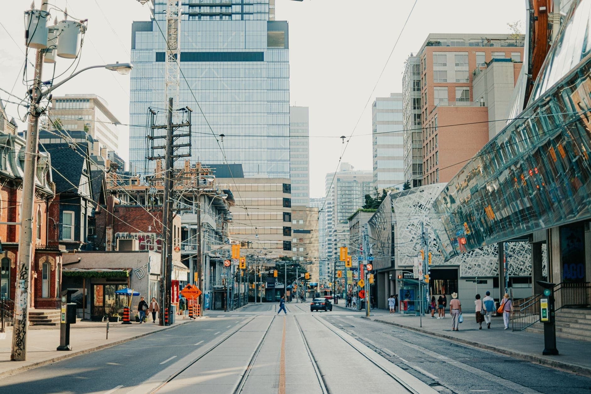 A sunny Toronto street with modern buildings, tram tracks, people walking, and city architectural mix in the downtown core.
