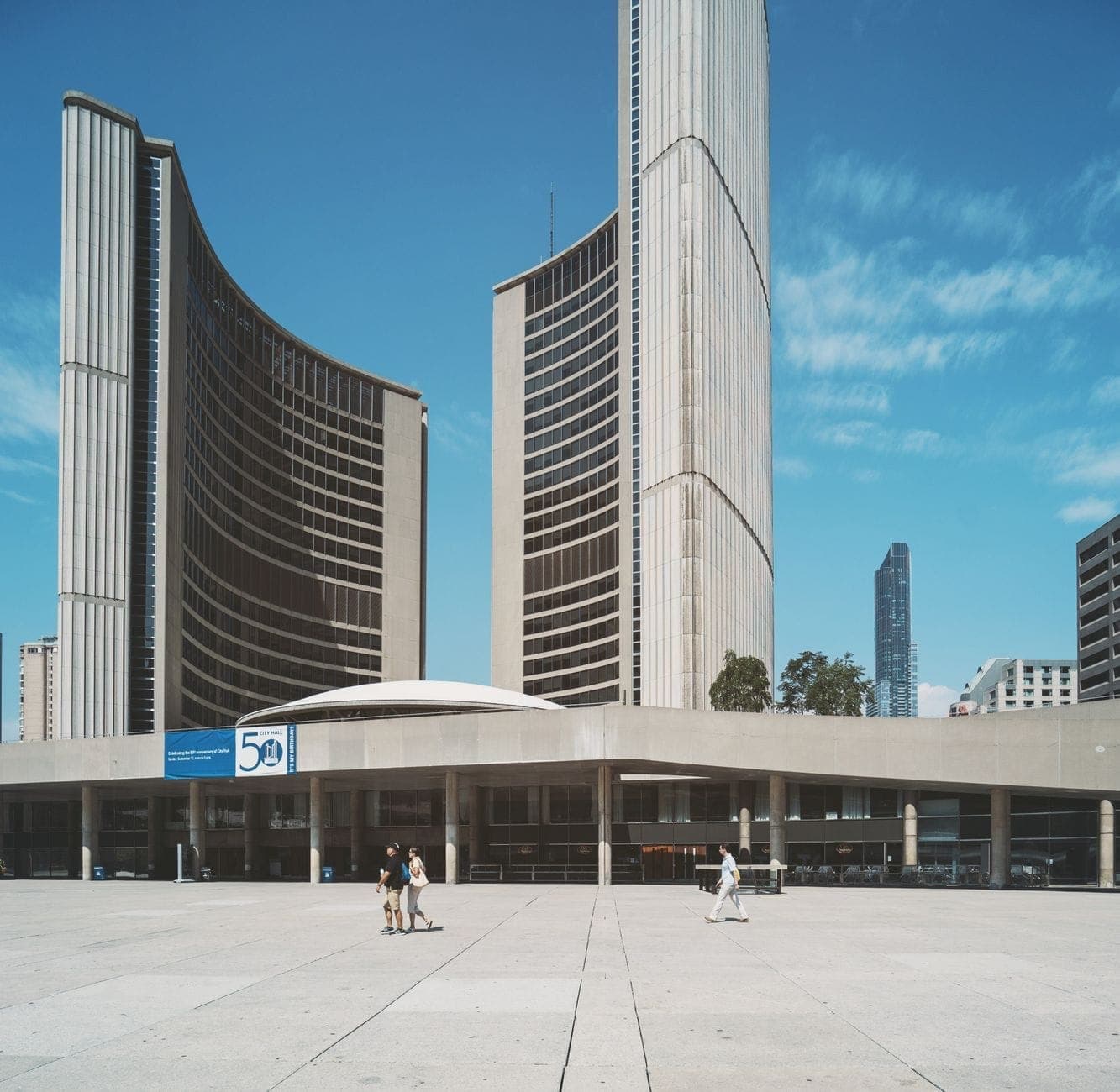 Toronto City Hall on a sunny day with distinctive curved towers and people walking across Nathan Phillips Square.