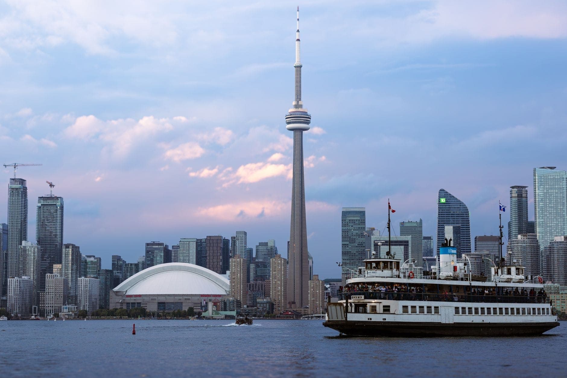 Il traghetto dell'Harbour Star attraversa il porto di Toronto al crepuscolo, con la skyline del centro e la CN Tower sullo sfondo.