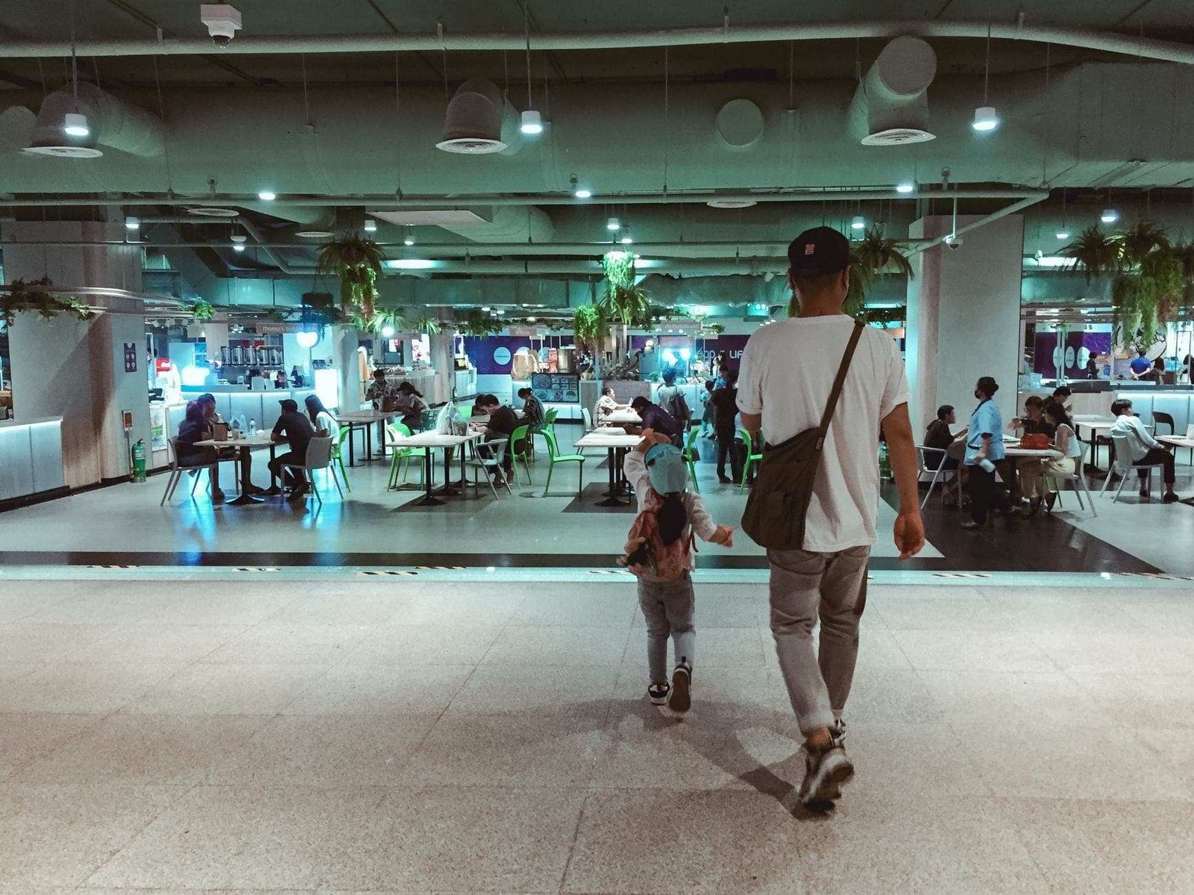 People sitting and dining at tables in a modern, well-lit underground food court with various eateries in the background.