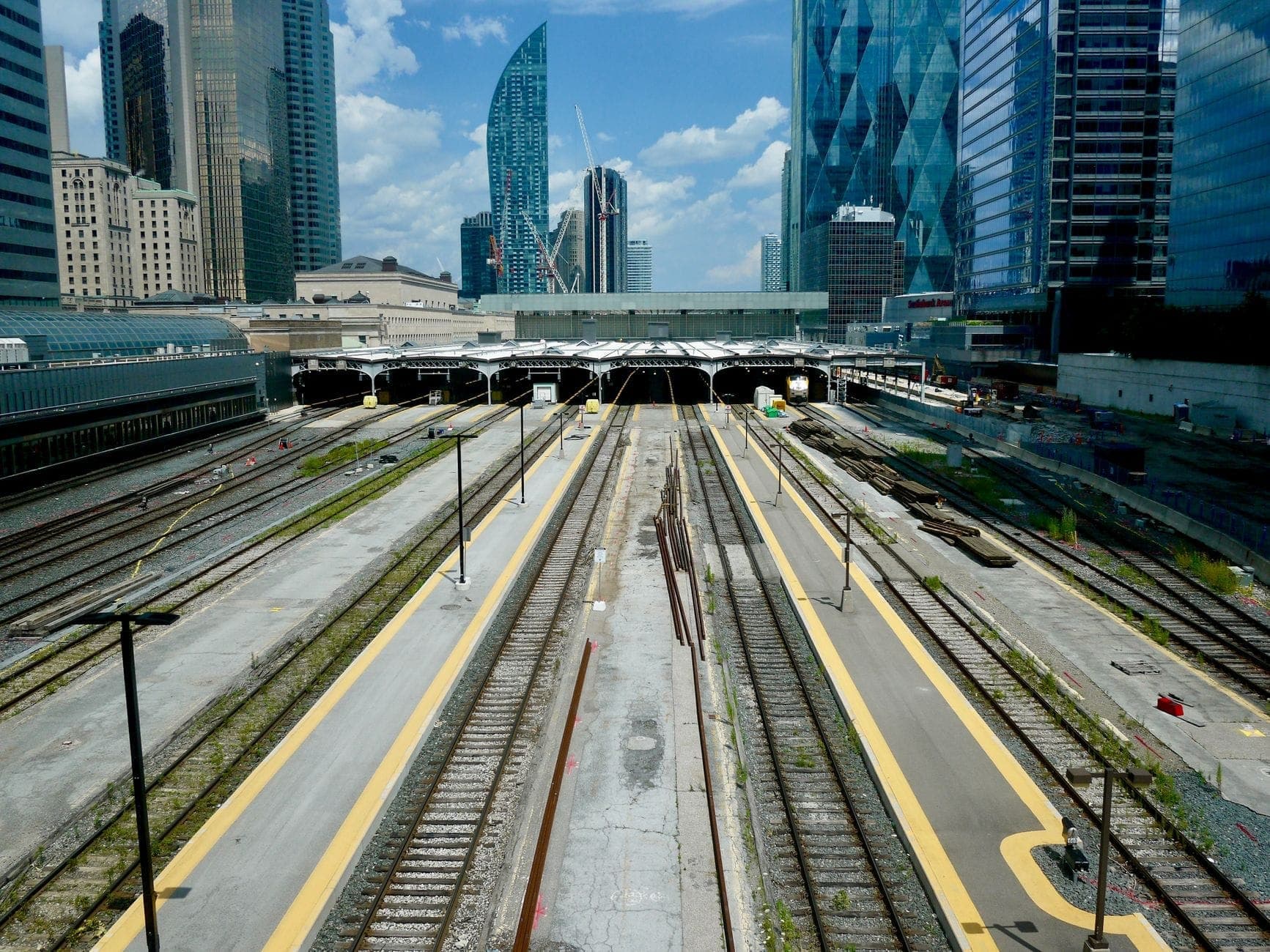 View of railway tracks leading into Toronto Union Station with downtown skyscrapers in the background on a sunny day.