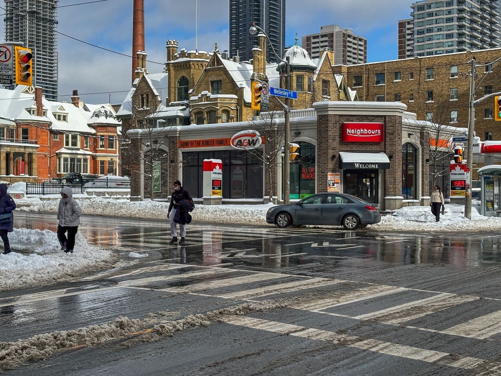 Snowy Toronto street intersection with pedestrians crossing, cars, mid-rise historic and modern buildings in winter, showing why PATH might be useful.