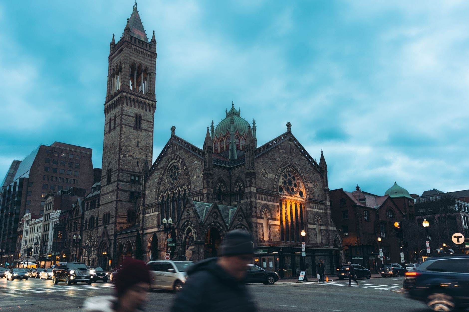 La Trinity Church de Boston à Copley Square au crépuscule, son architecture néo-romane illuminée se détachant sur l'animation de la rue au premier plan.