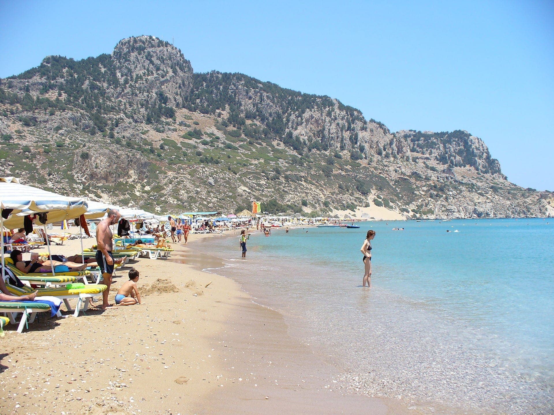 La plage de Tsambika avec son sable doré, ses transats et des personnes profitant de l'eau turquoise claire sous des collines spectaculaires sur la côte est de Rhodes.