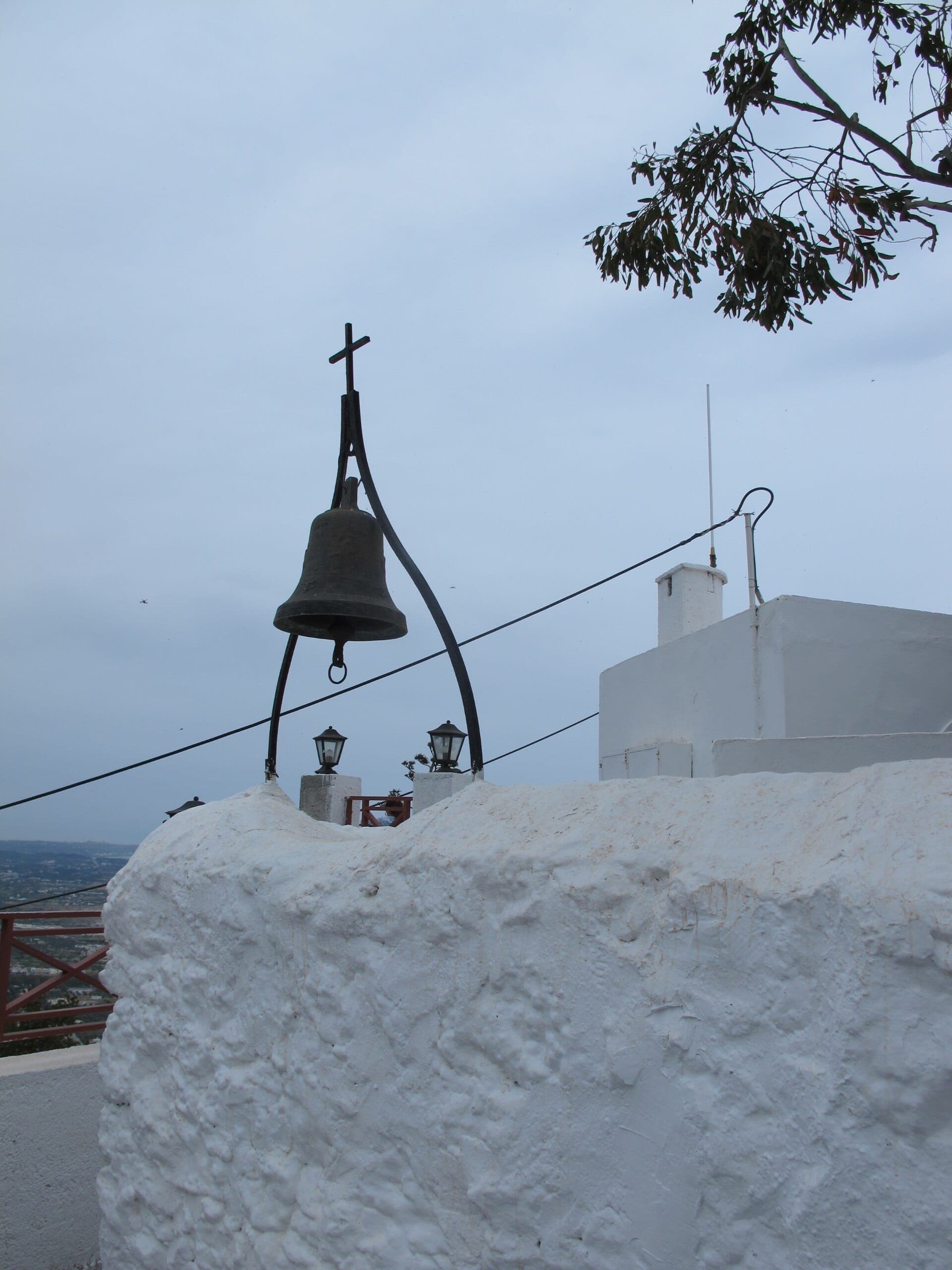 Gros plan des murs en pierre blanchis à la chaux du Monastère de Tsambika avec une cloche d'église et une croix sur un ciel nuageux à Rhodes.