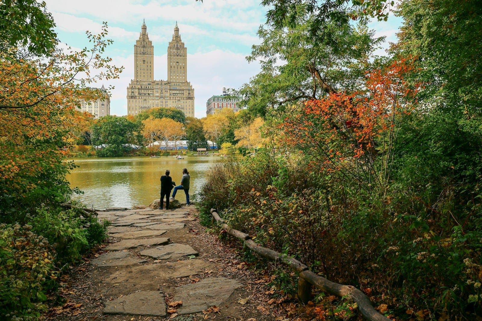 เส้นทางเดินใน Central Park มองไปเห็นขอบฟ้า Upper West Side กับใบไม้เปลี่ยนสีและผู้คนกำลังเดินเล่นริมสระน้ำกลางนิวยอร์ก