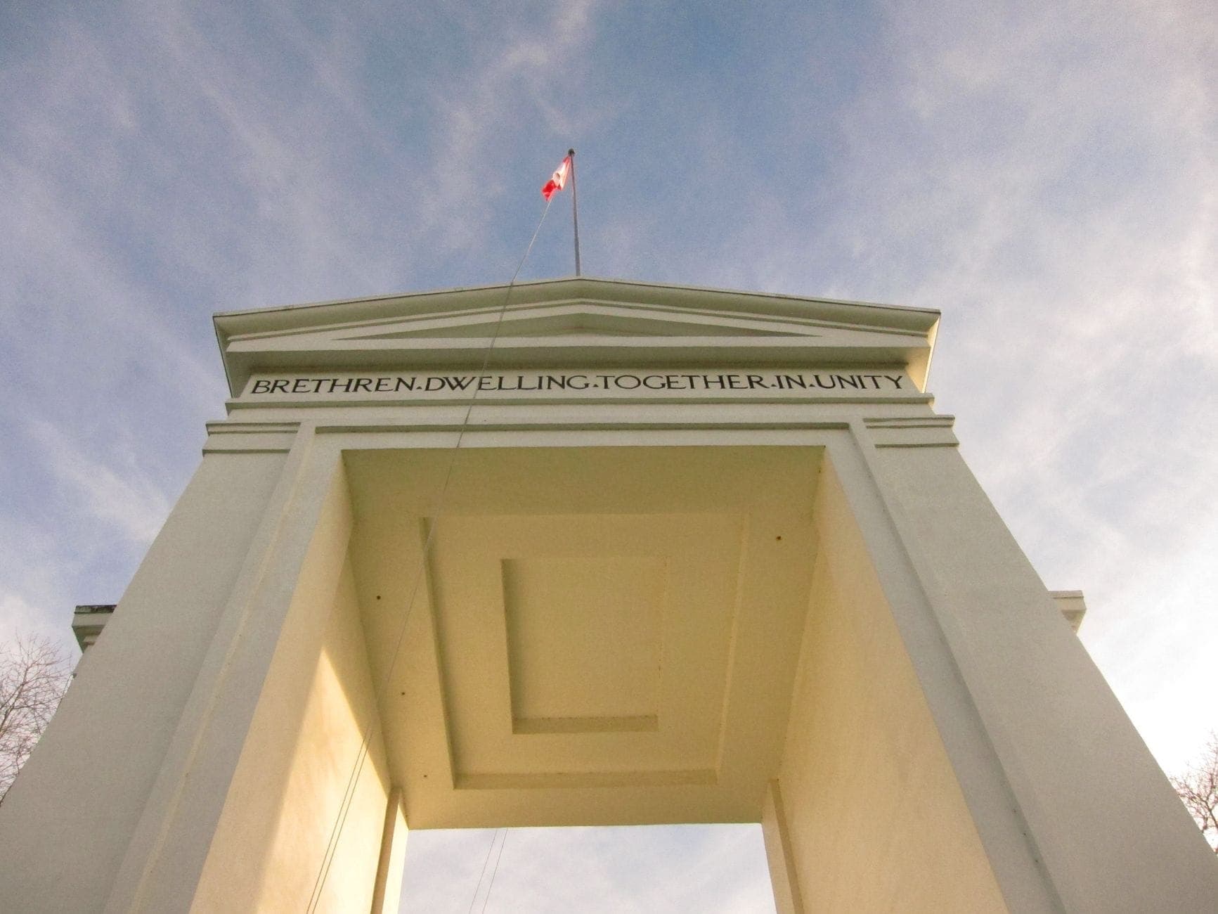 มุมมองจากด้านล่างขึ้นไปยังอนุสาวรีย์ Peace Arch ที่ชายแดนแคนาดา-สหรัฐอเมริกา พร้อมธงชาติแคนาดาอยู่ด้านบนและท้องฟ้าสีฟ้าเหนือขึ้นไป