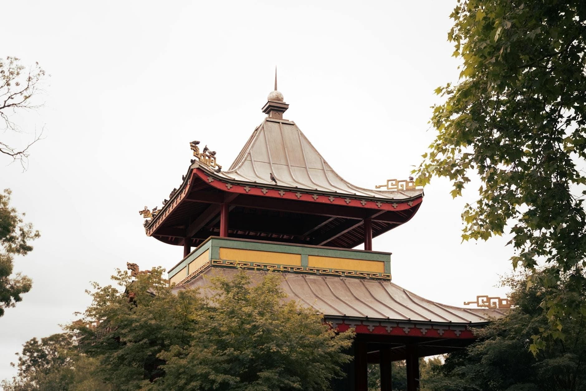 Un pabellón de estilo chino tradicional rodeado de árboles verdes en Victoria Park, East End de Londres, bajo un cielo nublado.