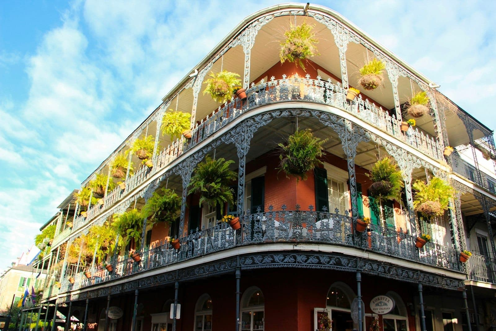 Historic Vieux Carré building with intricate wrought-iron balconies and hanging plants under a bright blue sky in New Orleans’ French Quarter.