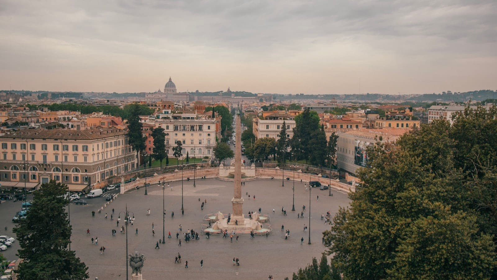 Panoramikong tanawin ng Piazza del Popolo at ng skyline ng lungsod mula sa terrasa ng Pincio sa Roma, na may mga puno at gusali sa ilalim ng malambot na ulap.