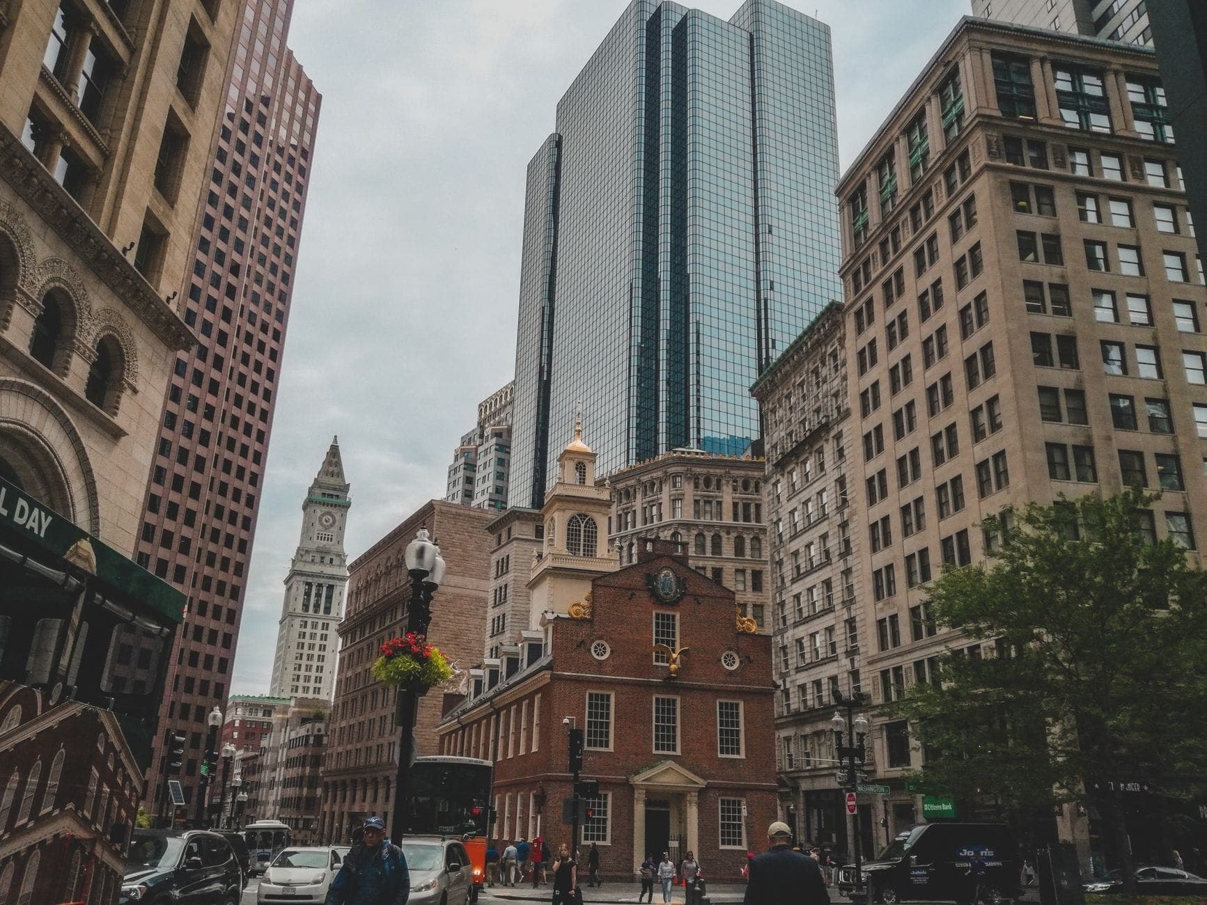 Vue au niveau de la rue du centre-ville de Boston avec des promeneurs, le Old State House historique, des gratte-ciel modernes et des monuments architecturaux sous un ciel nuageux.
