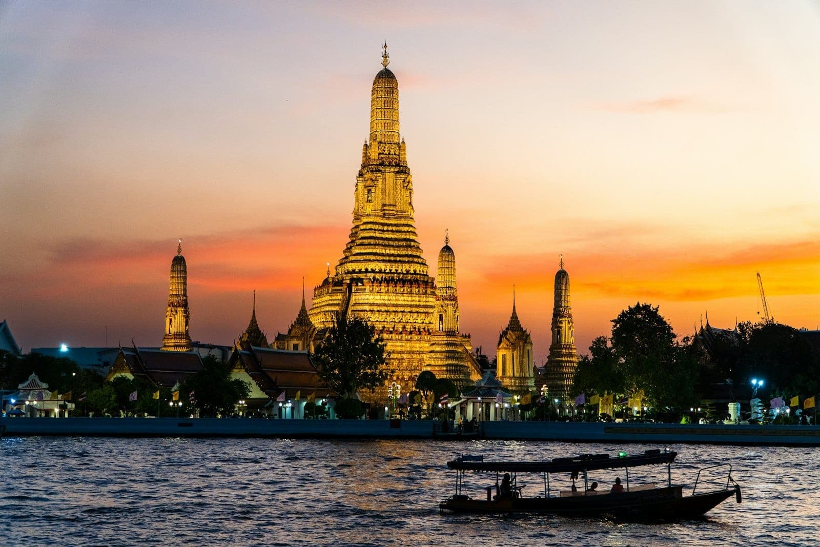 Wat Arun au coucher du soleil vu depuis le Chao Phraya à Bangkok avec un bateau traditionnel au premier plan