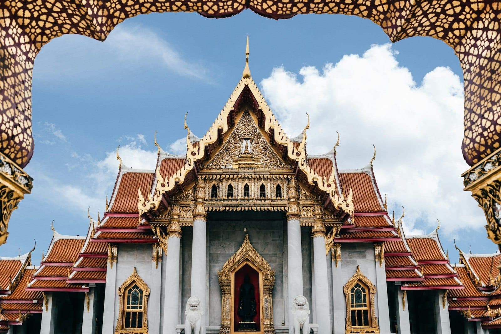 Majestic Wat Benchamabophit temple in Bangkok with white Carrara marble facade, ornate multi-tiered roofs, and guardian lion statues at the entrance.