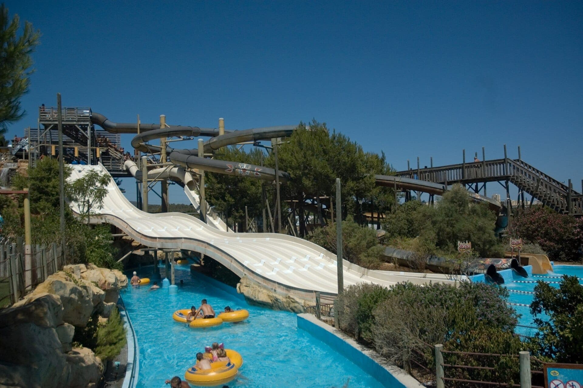 Breite Wasserrutschen und kurvenreiche Röhrenfahrten im Western Water Park Magaluf, mit Familien auf gelben Schwimmringen bei strahlendem Sonnenschein.