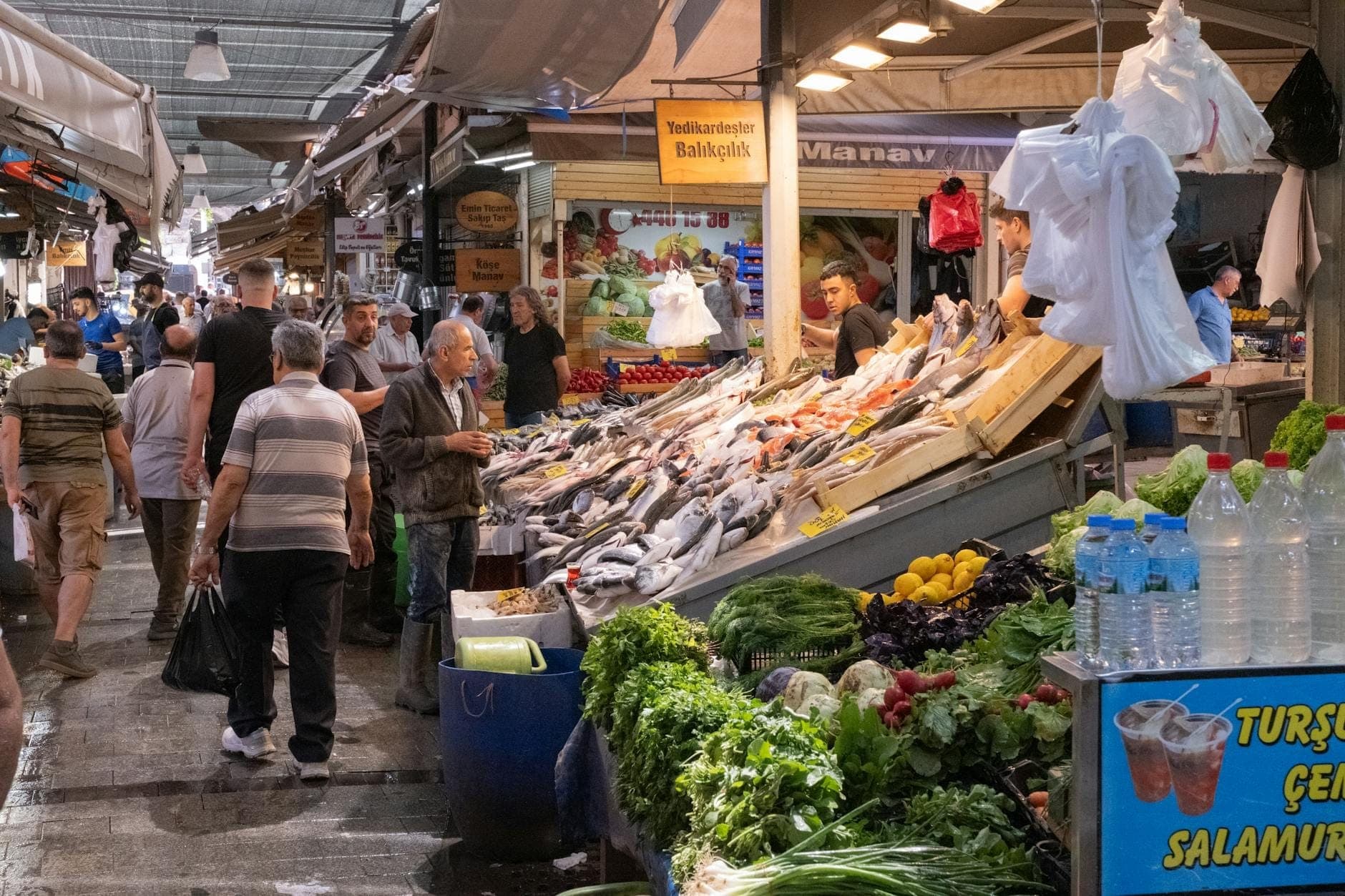 Lebhafte Marktszene in Antalya mit Einheimischen, frischem Fisch, Gemüse und türkischen Marktschildern unter überdachten Ständen.