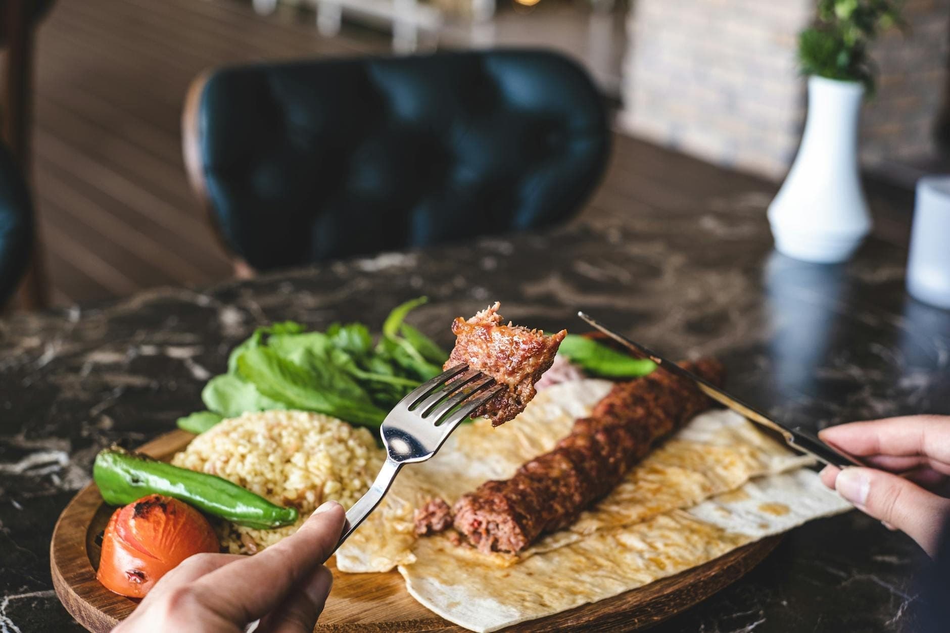 Nahaufnahme eines traditionellen türkischen Kebabs, serviert mit Fladenbrot, gegrilltem Gemüse, frischen Kräutern und Bulgur auf einem Holztablett in einem stilvollen Antalya-Restaurant.