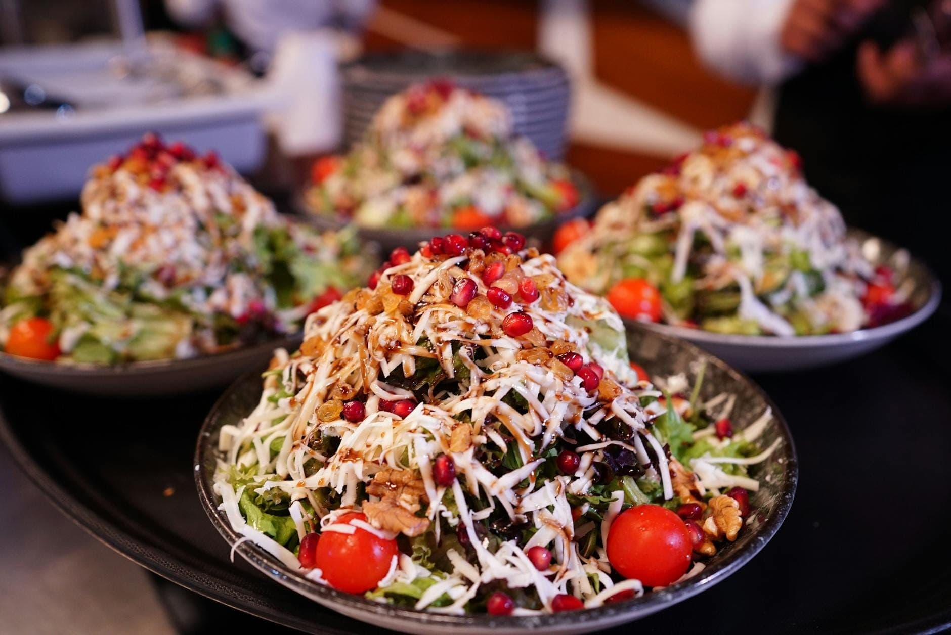 Vier reich belegte Teller mit türkischen Salaten, darunter Granatapfelkerne, Walnüsse, Kirschtomaten und geraspelter Weißkäse. Lebhafte Präsentation im Familienstil in einem Restaurant.