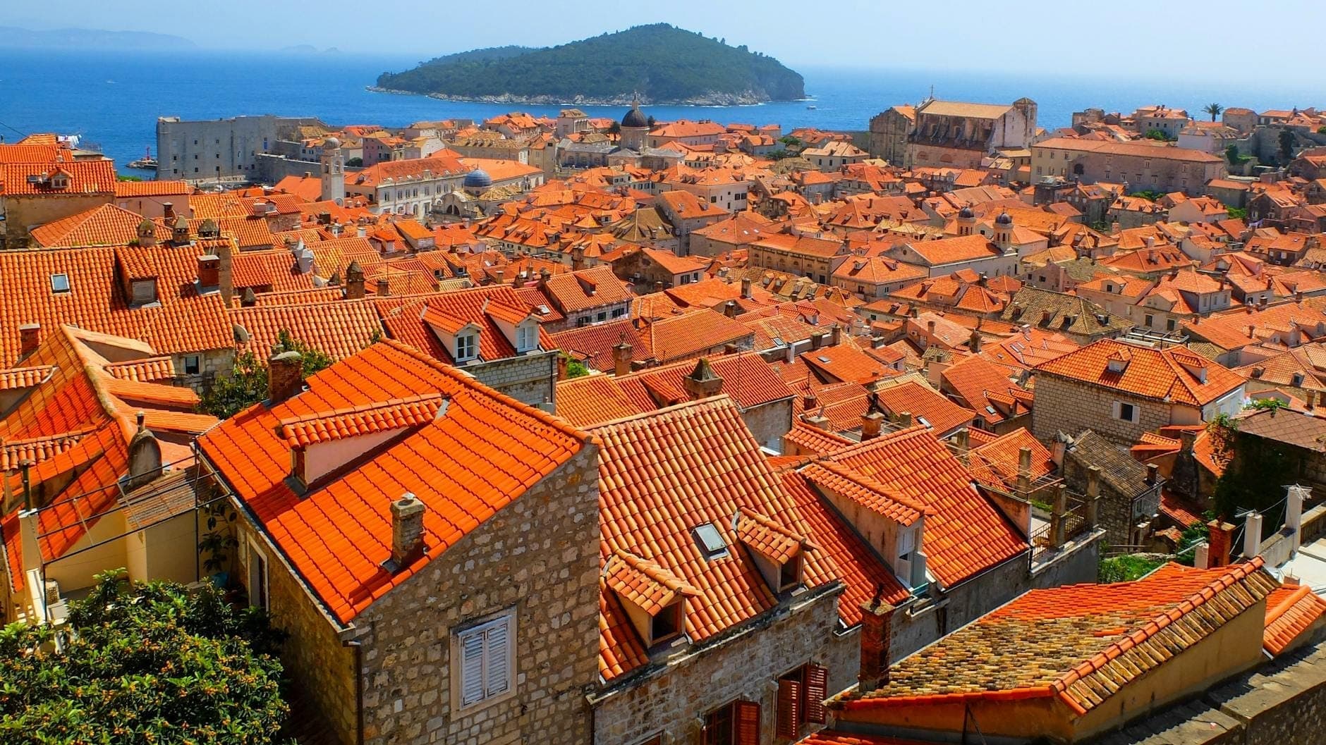 Lebhaftes Panorama über Dubrovniks Altstadt mit roten Dächern, Steingebäuden und der Adria im Hintergrund an einem klaren, sonnigen Tag.