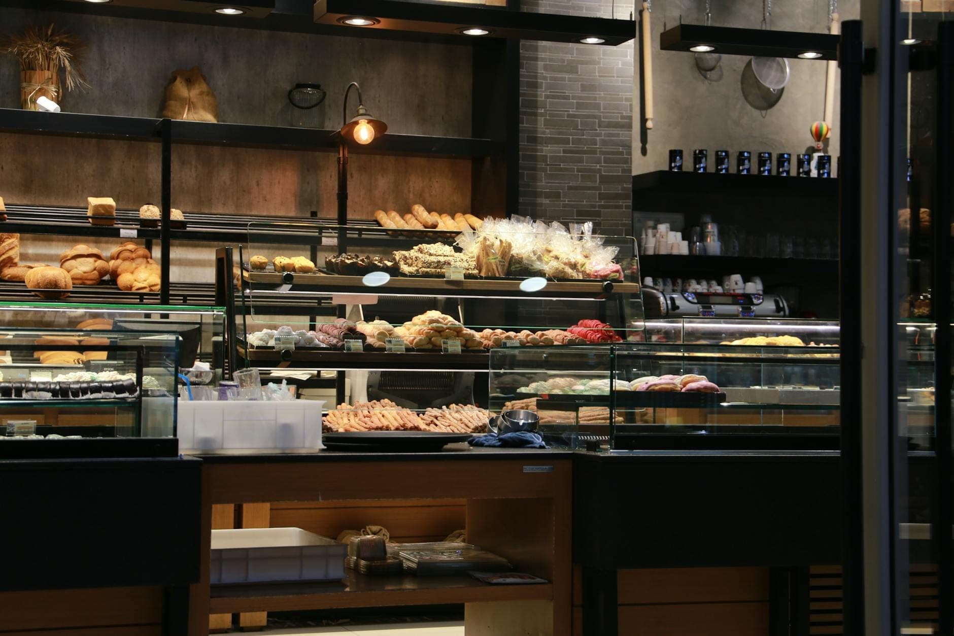 Intérieur d'une boulangerie avec des vitrines en verre remplies de pains et de pâtisseries, un éclairage chaleureux et une décoration rustique.