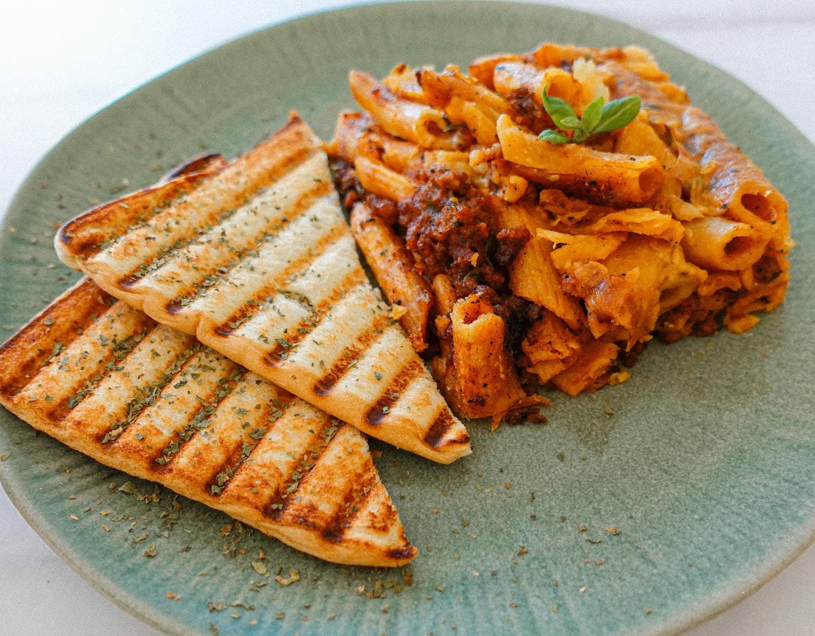 Plato de rigatoni al horno con salsa de carne roja, servido con dos trozos de pan a la parrilla.