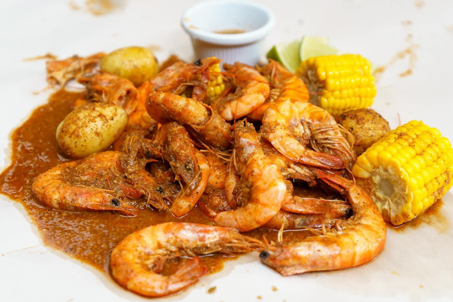 A close-up of a Cajun seafood boil with shrimp, potatoes, corn on the cob, and sauce on a white table.