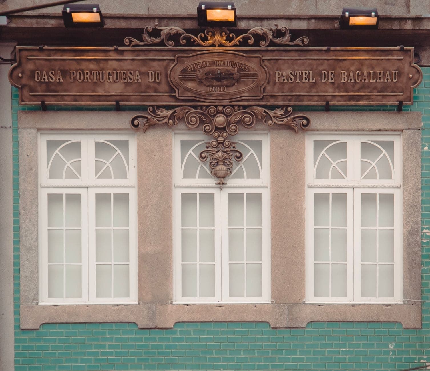 Fachada de Casa Portuguesa do Pastel de Bacalhau, una tienda especializada en bocados de bacalao salado en Porto, con su ornamentado letrero sobre el exterior de azulejos verdes.