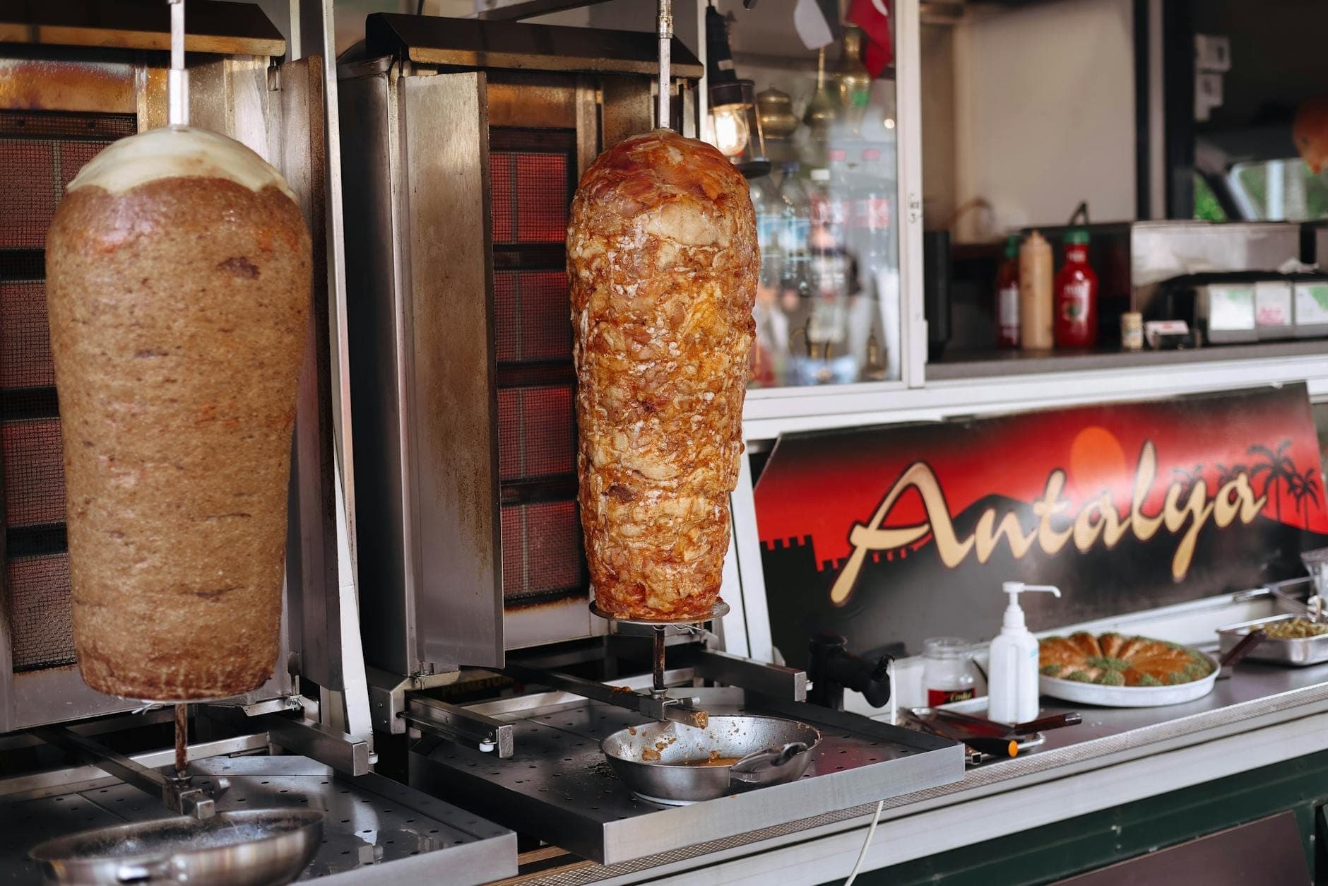 Viande de döner kebab tournant sur des broches dans un stand de street food, avec un panneau indiquant 'Antalya' en arrière-plan.