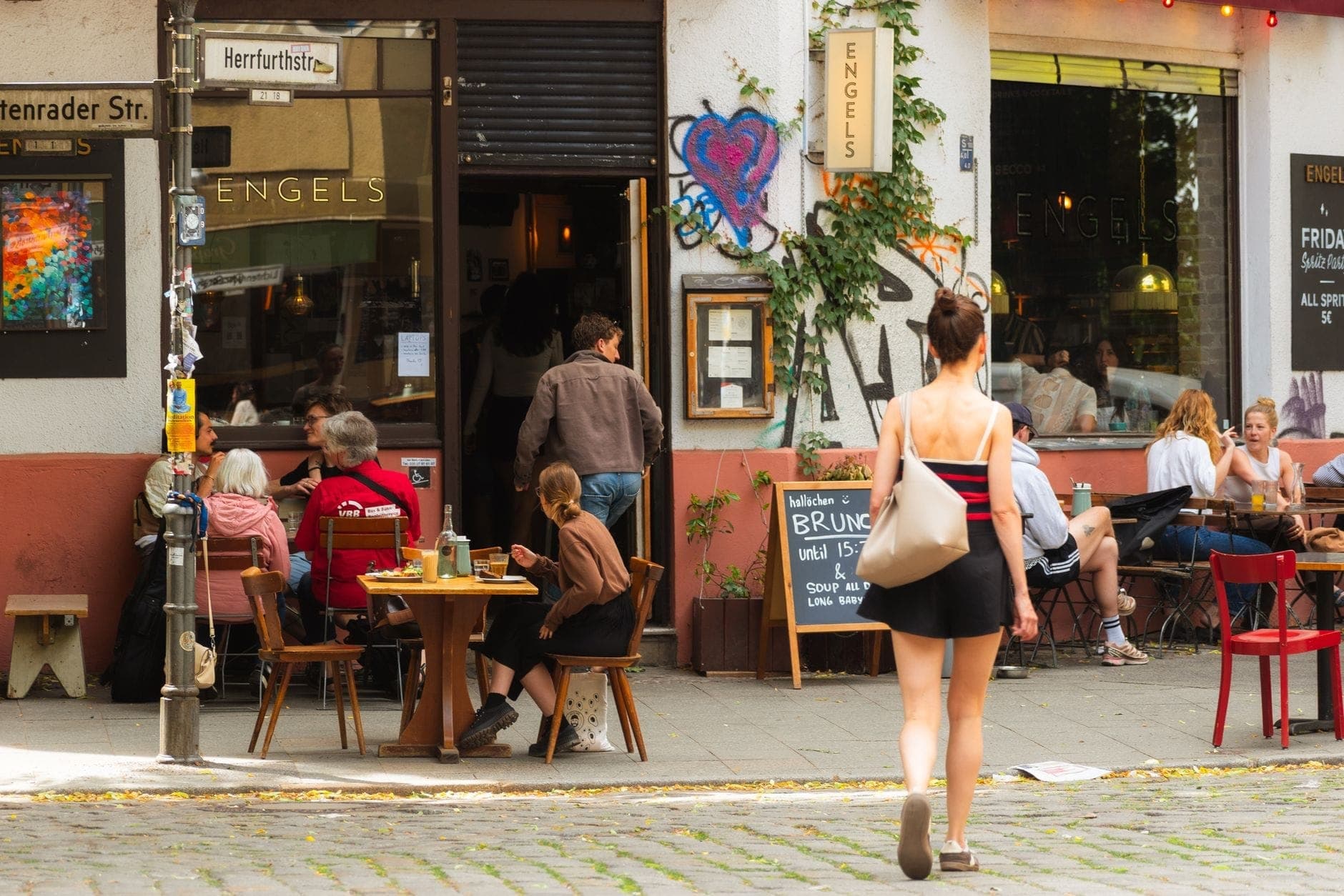 Animado café de calle en Berlín con personas comiendo al aire libre frente a un colorido y ligeramente descuidado restaurante de barrio.