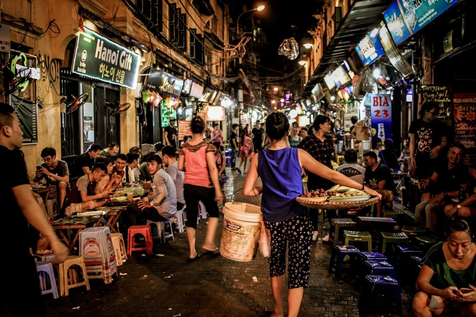 Tętniąca życiem nocna scena street foodowa w Hanoi – miejscowi i turyści jedzą na małych stołeczkach, wśród kolorowych świateł i gwarnych straganów z jedzeniem.