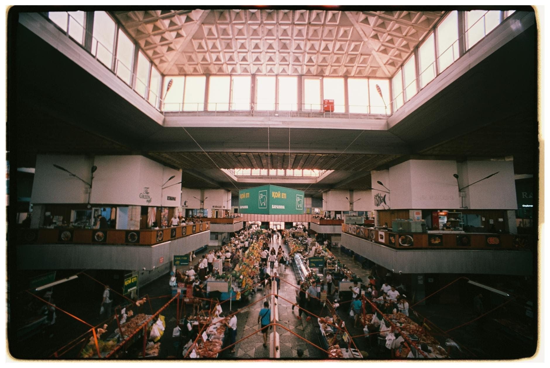 Vista ampla de um movimentado mercado coberto em Lisboa, com bancas de comida, teto alto e pessoas a fazer compras e a passear.