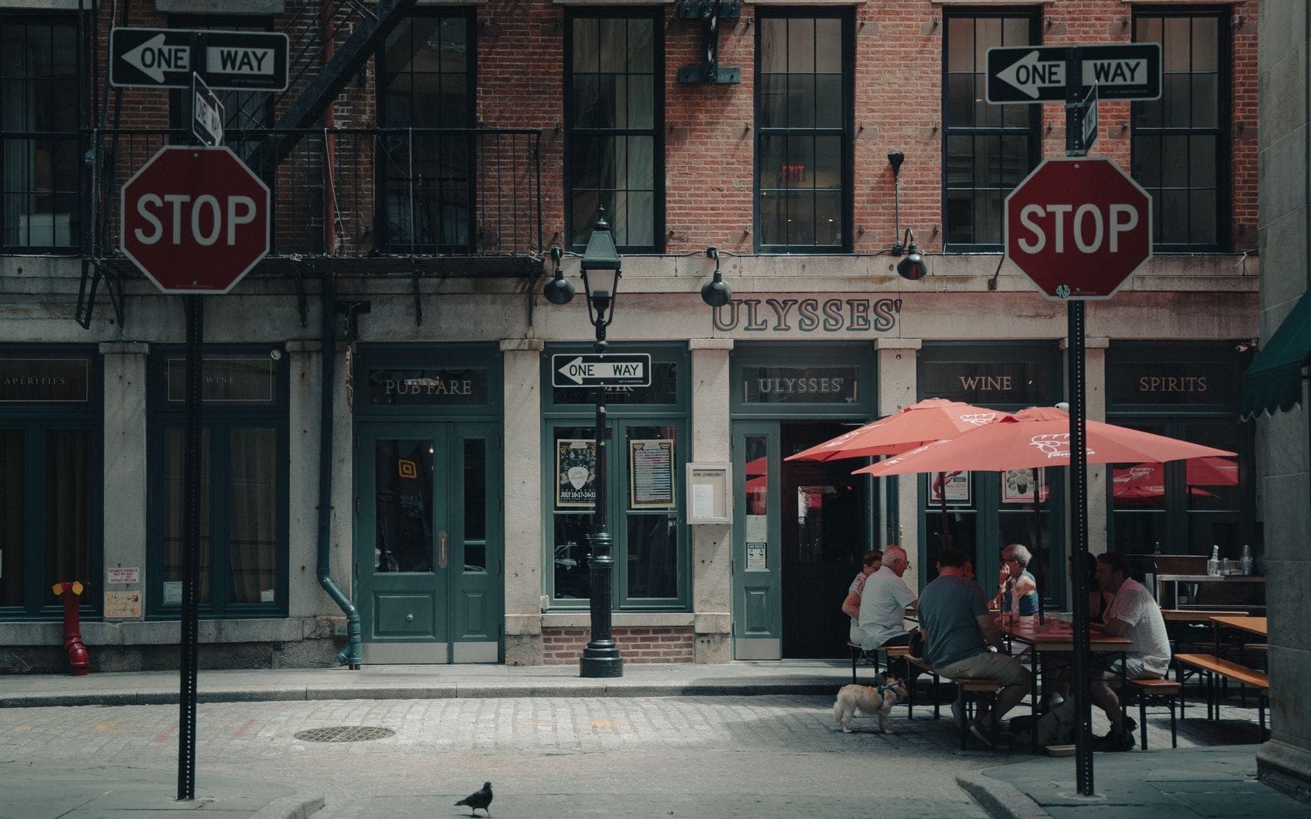 ผู้คนรับประทานอาหารกลางแจ้งที่ร้านอาหารใต้ร่มสีแดงบนถนนใน New York City ท่ามกลางอาคารอิฐสไตล์คลาสสิก