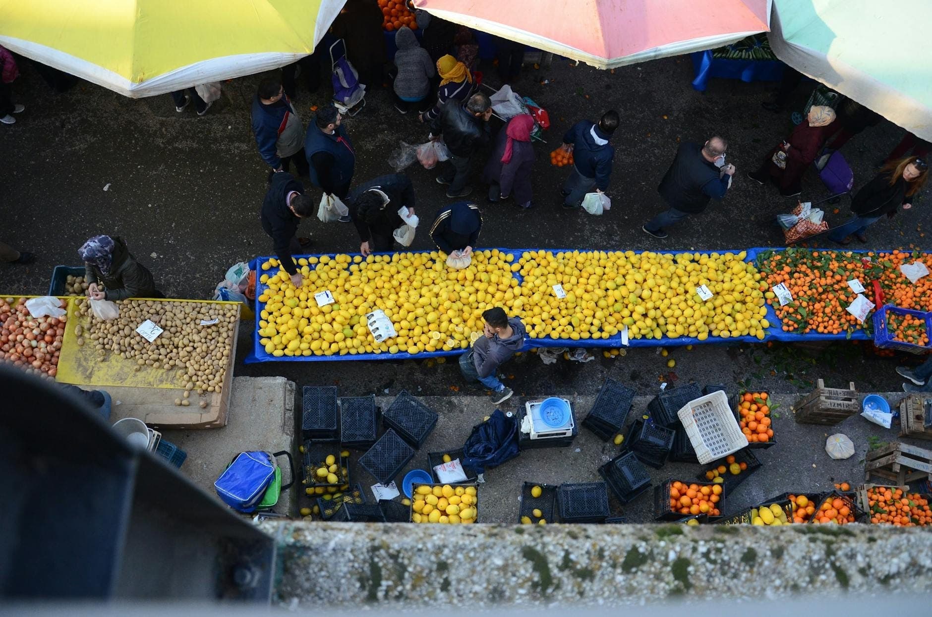 Overhead view of a bustling outdoor market in Paris with people shopping at colorful produce stalls under umbrellas.