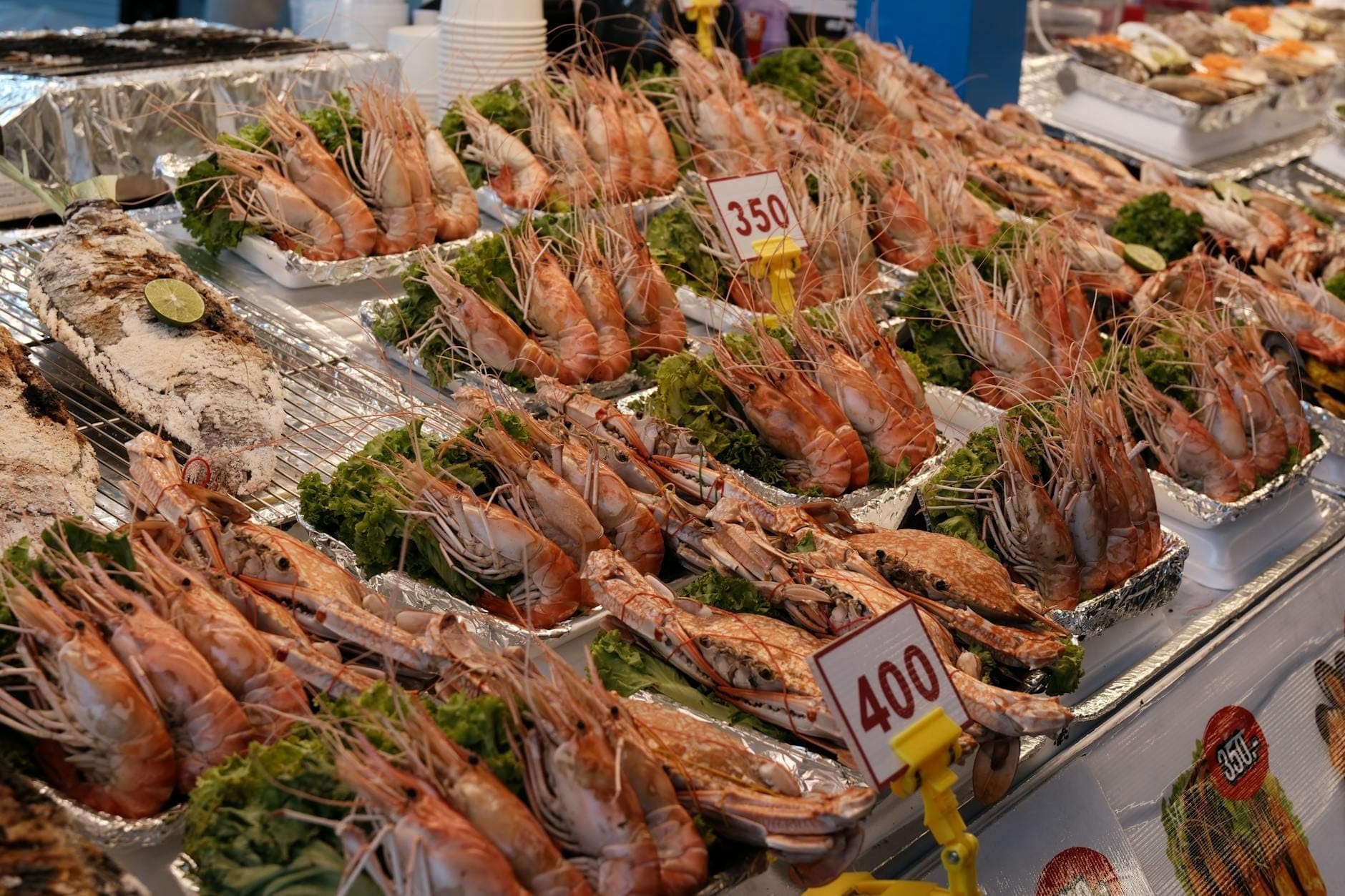Esposizione di gamberi tigre alla griglia e frutti di mare con cartellini dei prezzi in un affollato banco del mercato a Pattaya.