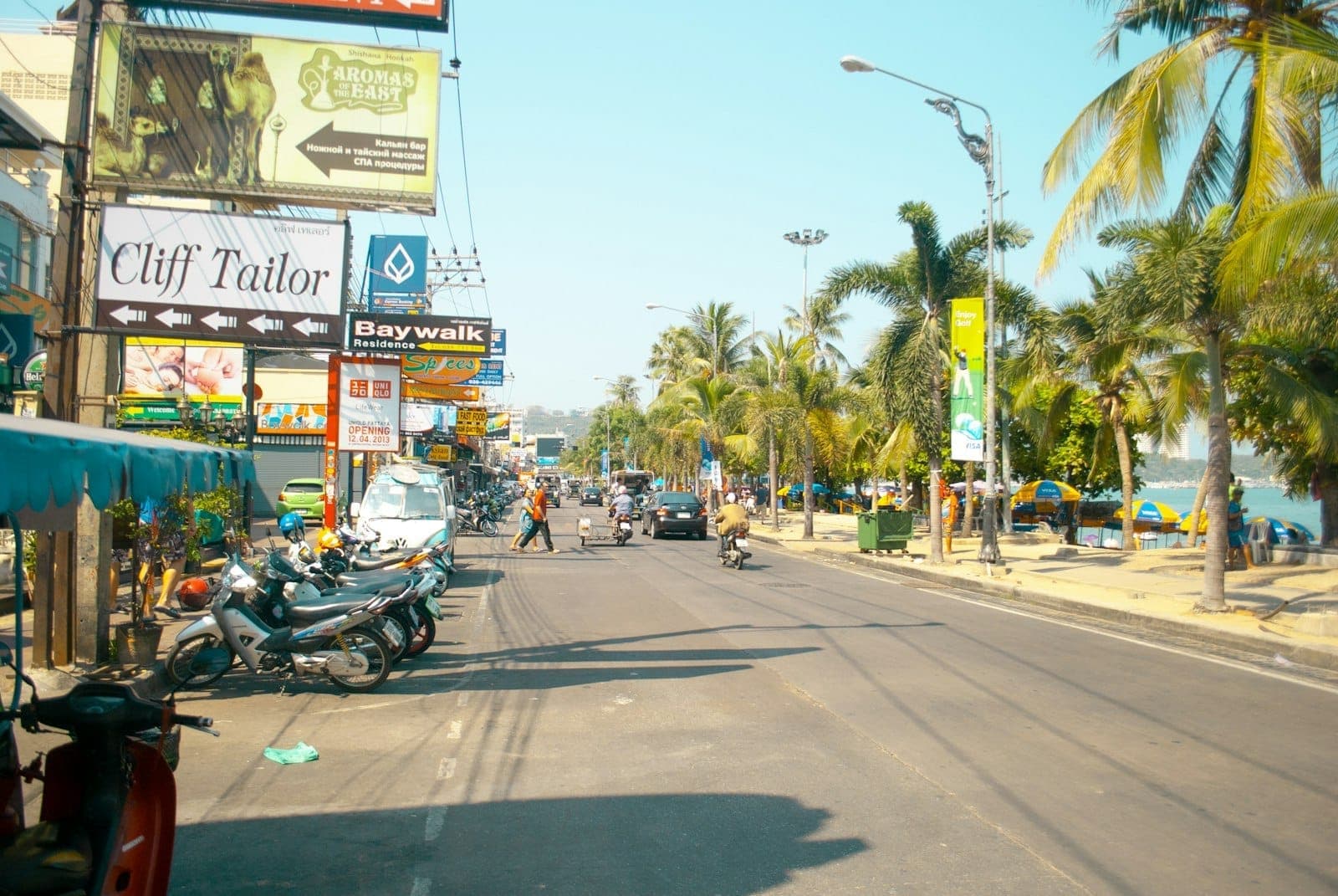 Una vivace strada a Pattaya fiancheggiata da ristoranti, attività locali, insegne di cibo, palme e persone che camminano vicino al lungomare.