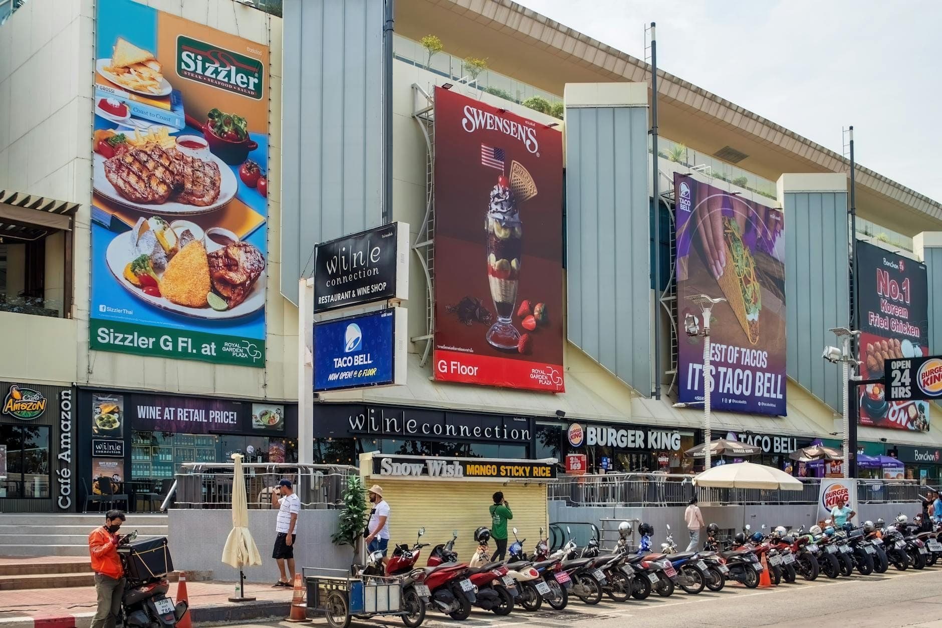 Vista stradale di un edificio moderno a Pattaya con grandi insegne per Sizzler, Swensen's, Burger King e Taco Bell, che mostra opzioni culinarie internazionali.
