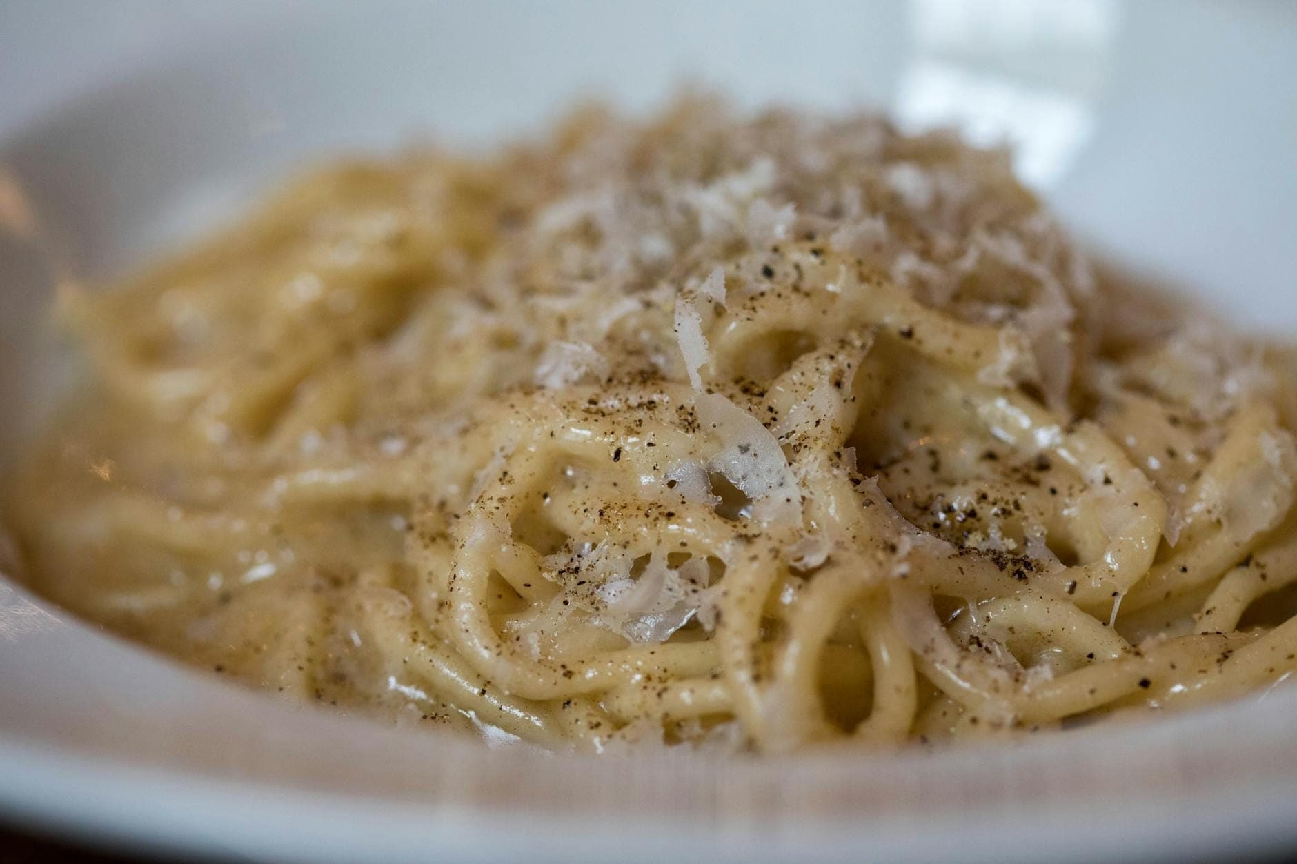 Nahaufnahme eines klassischen römischen Nudelgerichts, cacio e pepe, garniert mit schwarzem Pfeffer und Käse in einer weißen Schüssel.
