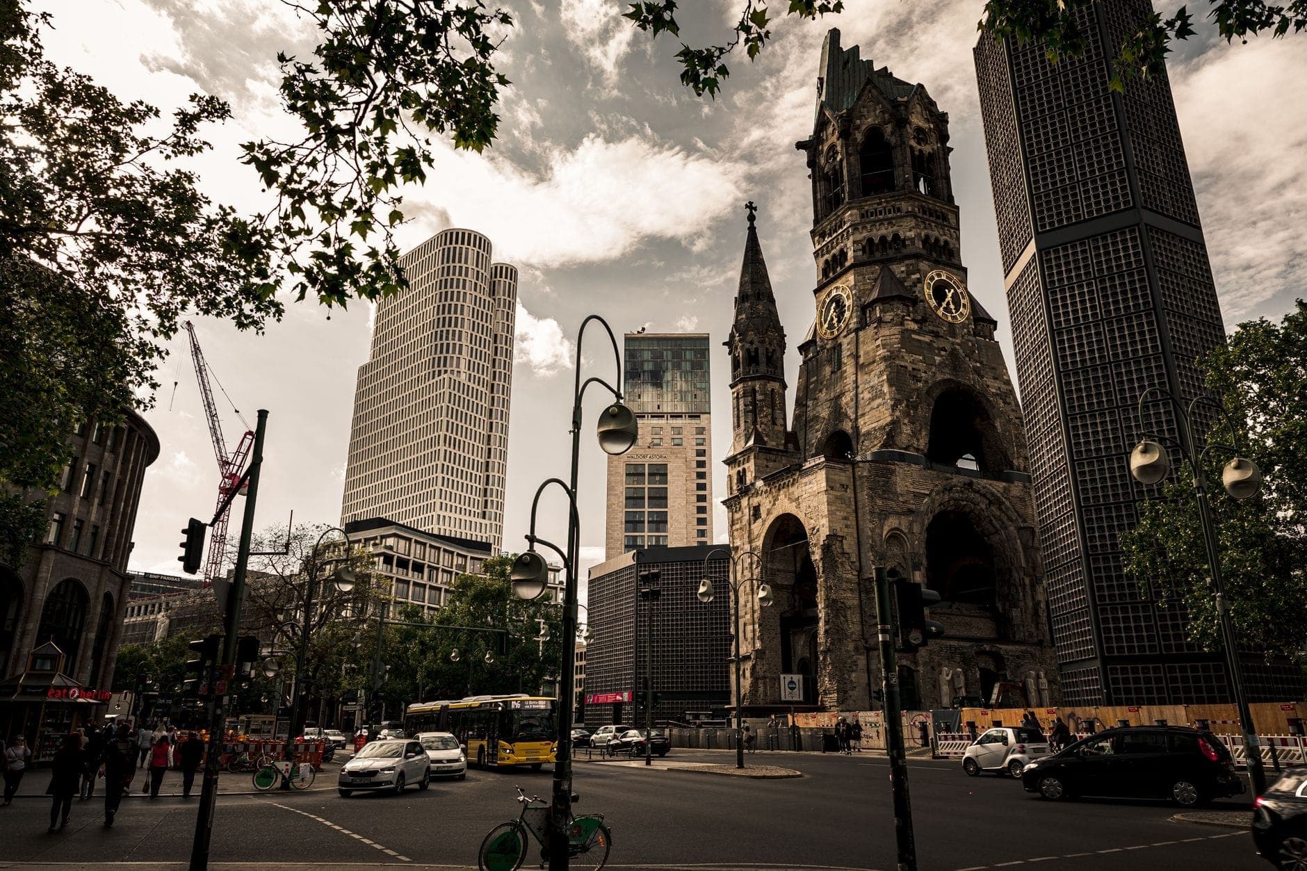 Vista ampla da Kaiser Wilhelm Memorial Church cercada por edifícios modernos e movimento nas ruas no bairro de Charlottenburg, em Berlim.