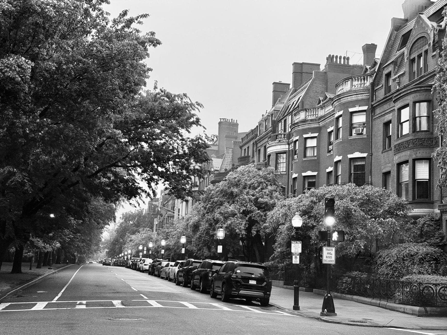 Photo en noir et blanc d'une rue bordée d'arbres avec des bâtiments historiques en grès brun et des voitures garées, typique du quartier Back Bay de Boston.