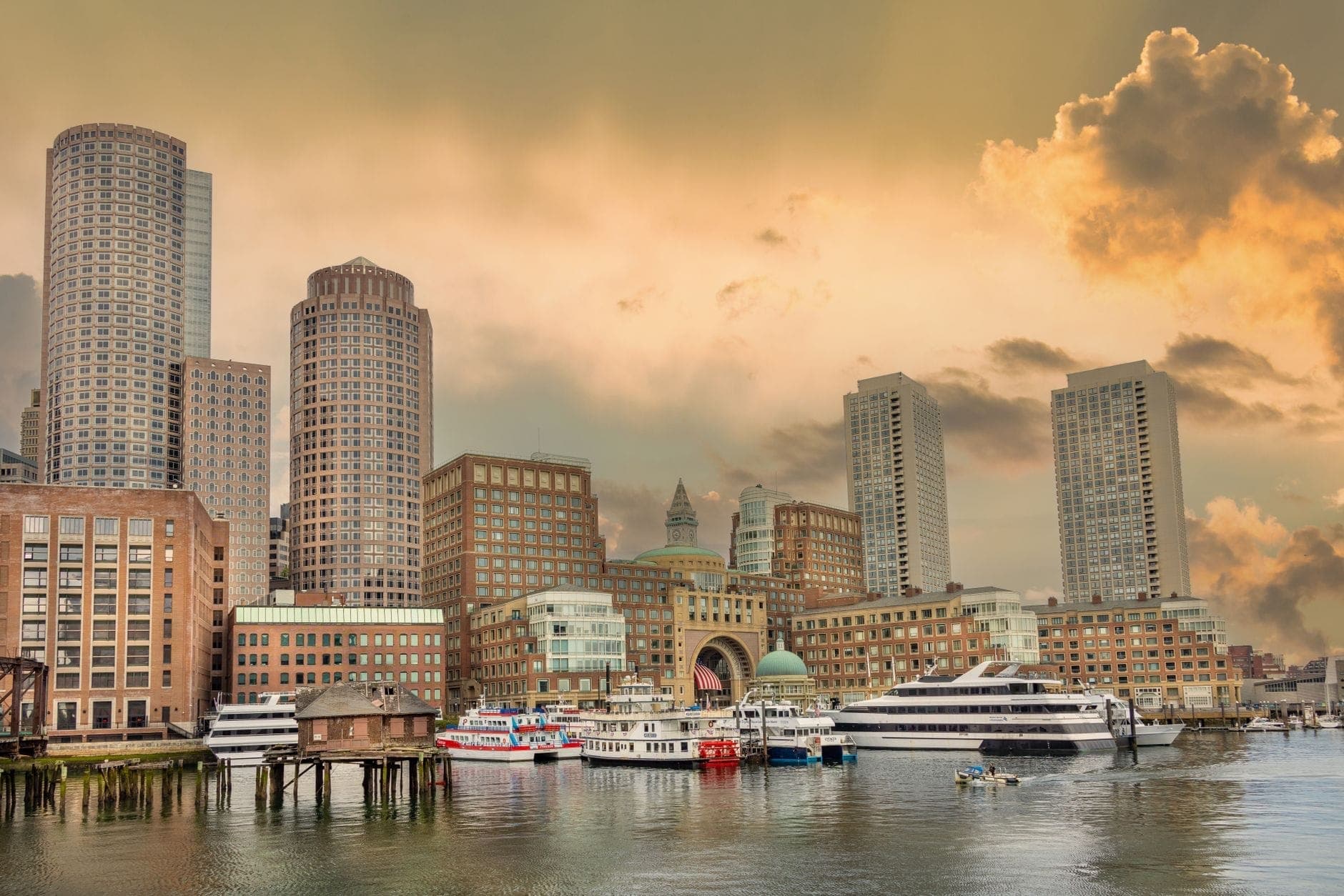 Horizon du Boston Seaport avec des gratte-ciel modernes, des hôtels en bord de mer, des vues sur le port et des bateaux amarrés au premier plan à la lumière du début de soirée.